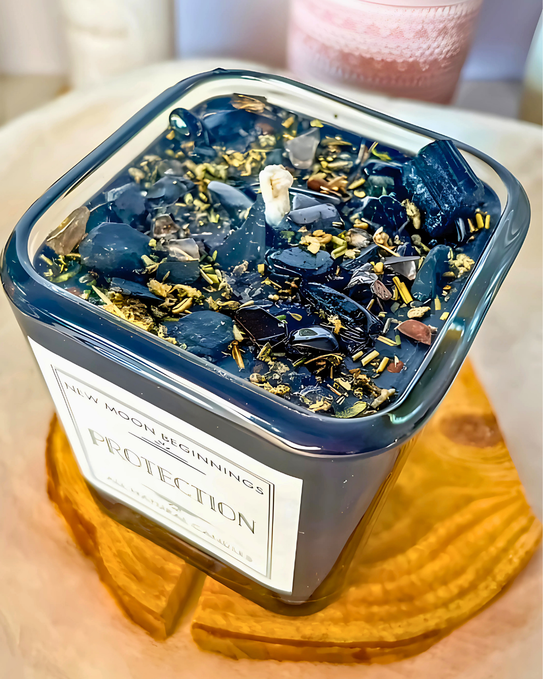 Candle in a container labeled 'Protection' with decorative elements on a wooden surface.