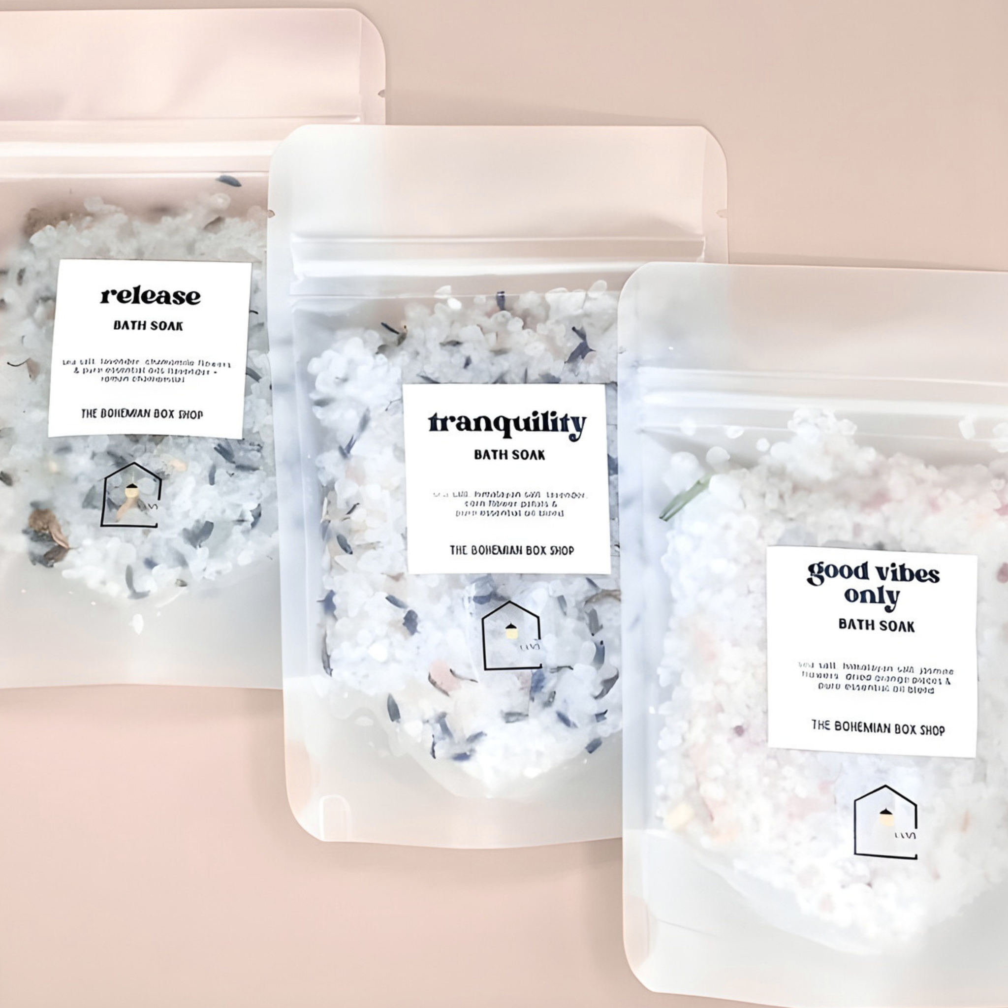 Three packages of bath soaks labeled 'release', 'tranquility', and 'good vibes only' on a light pink background.