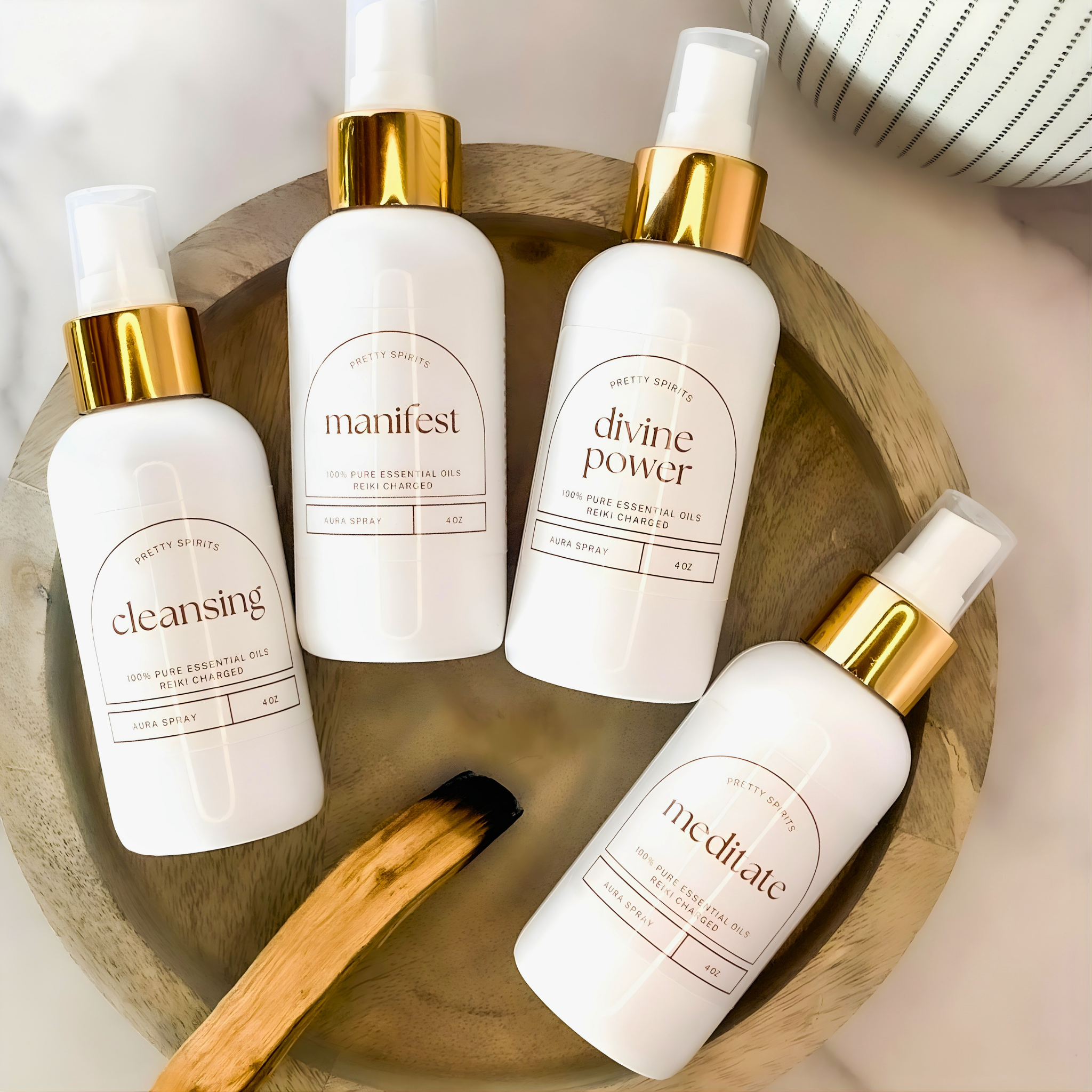 Four white bottles with gold caps on a wooden tray, featuring labels like 'manifest', 'divine power', and 'meditate'.