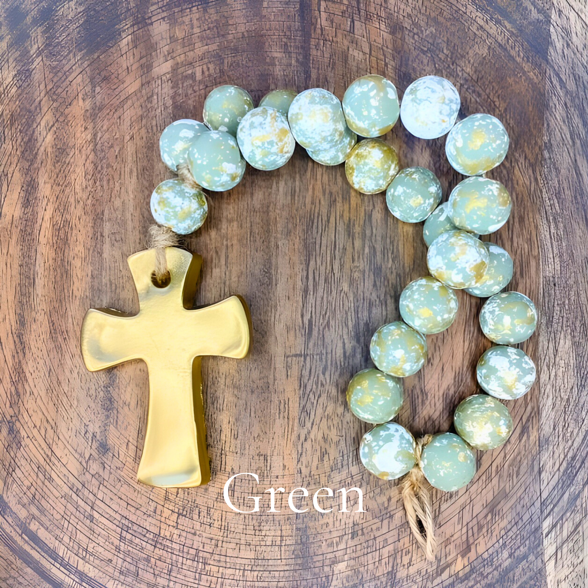 Green beaded necklace with a gold cross on a wooden surface