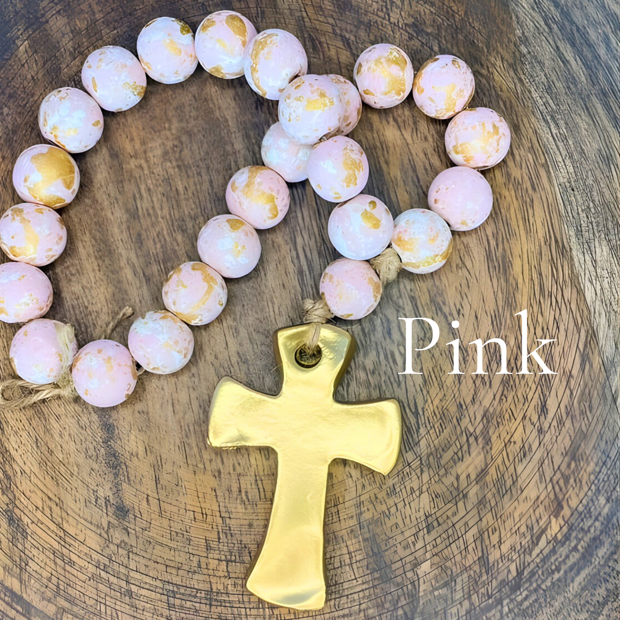 Pink beaded necklace with a gold cross on a wooden surface