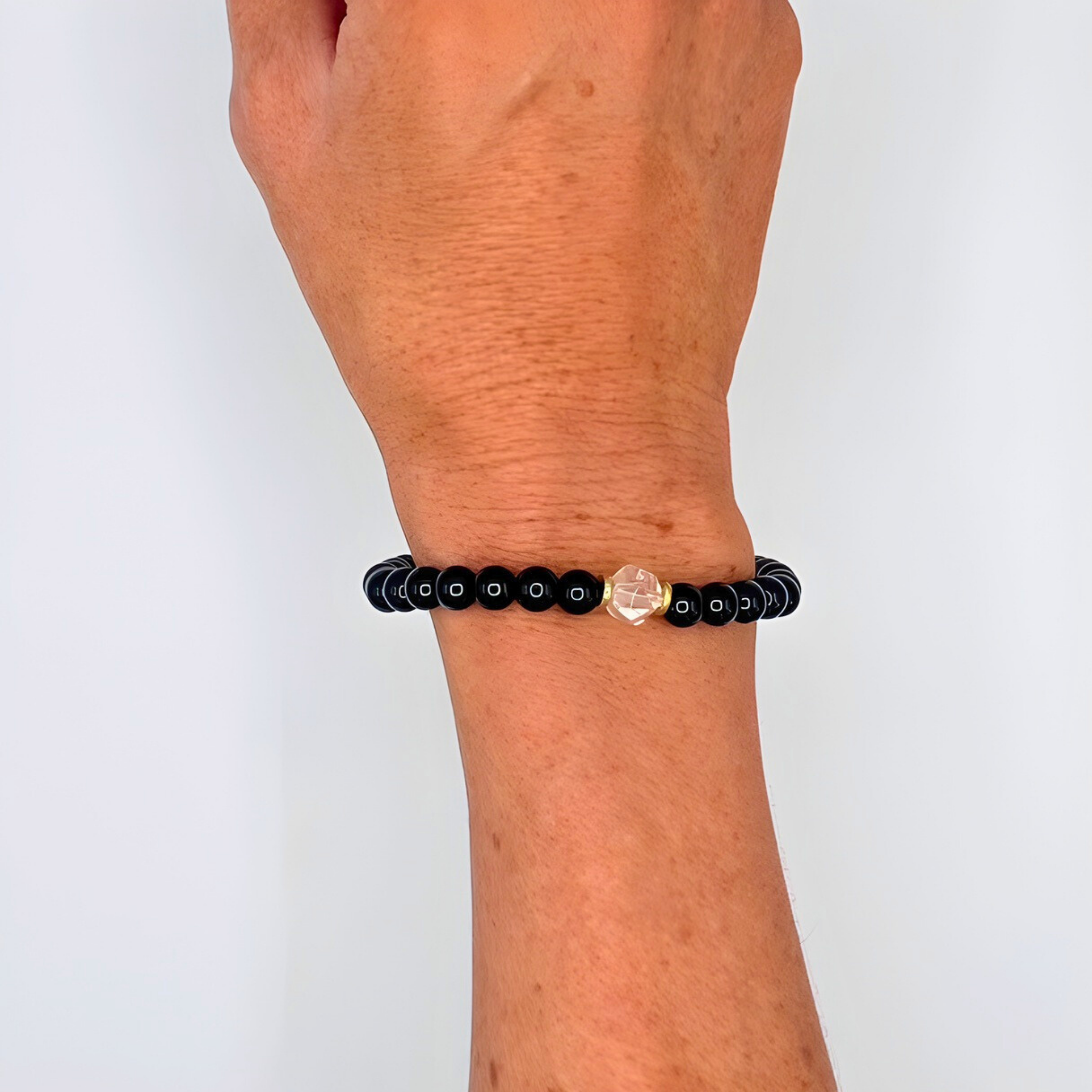 Black beaded bracelet with a clear crystal on a wrist against a white background