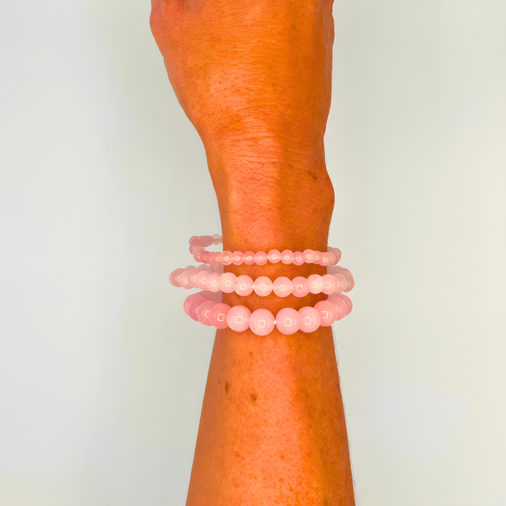 Wrist wearing three pink beaded bracelets on a plain background