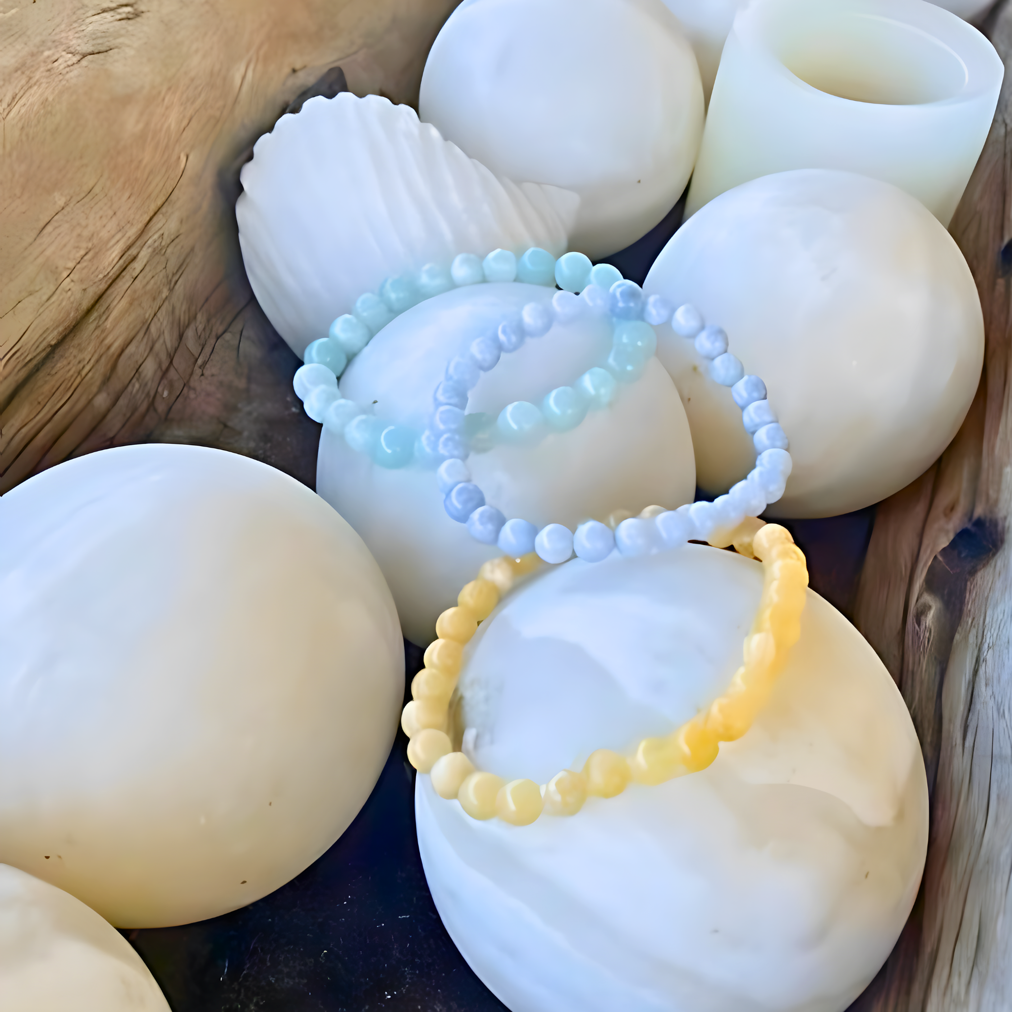 Two beaded bracelets, one yellow and one light blue, on white spherical objects with a wooden surface.