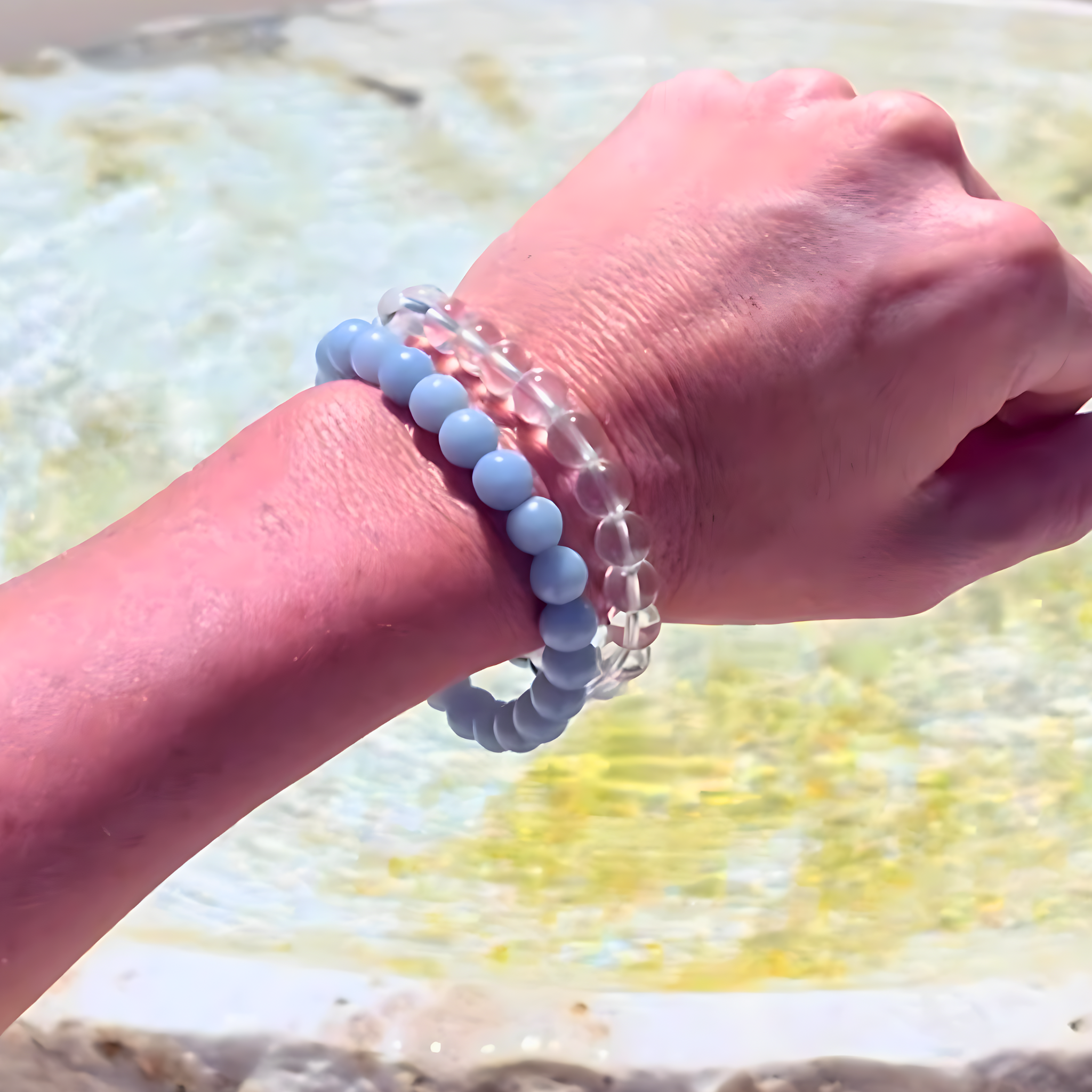 Hand wearing a bracelet with blue beads against a blurred natural background
