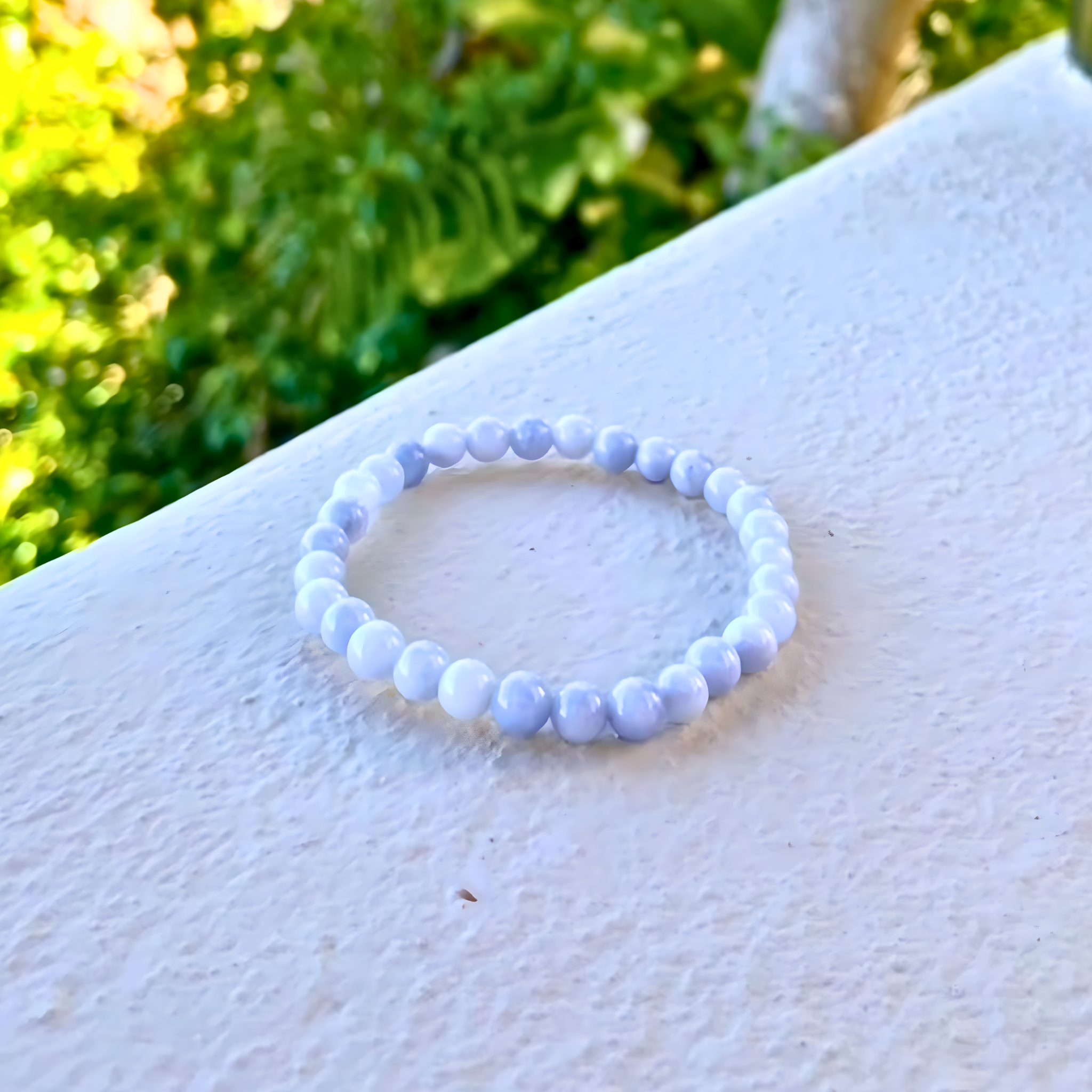 White beaded bracelet on a white surface with greenery in the background