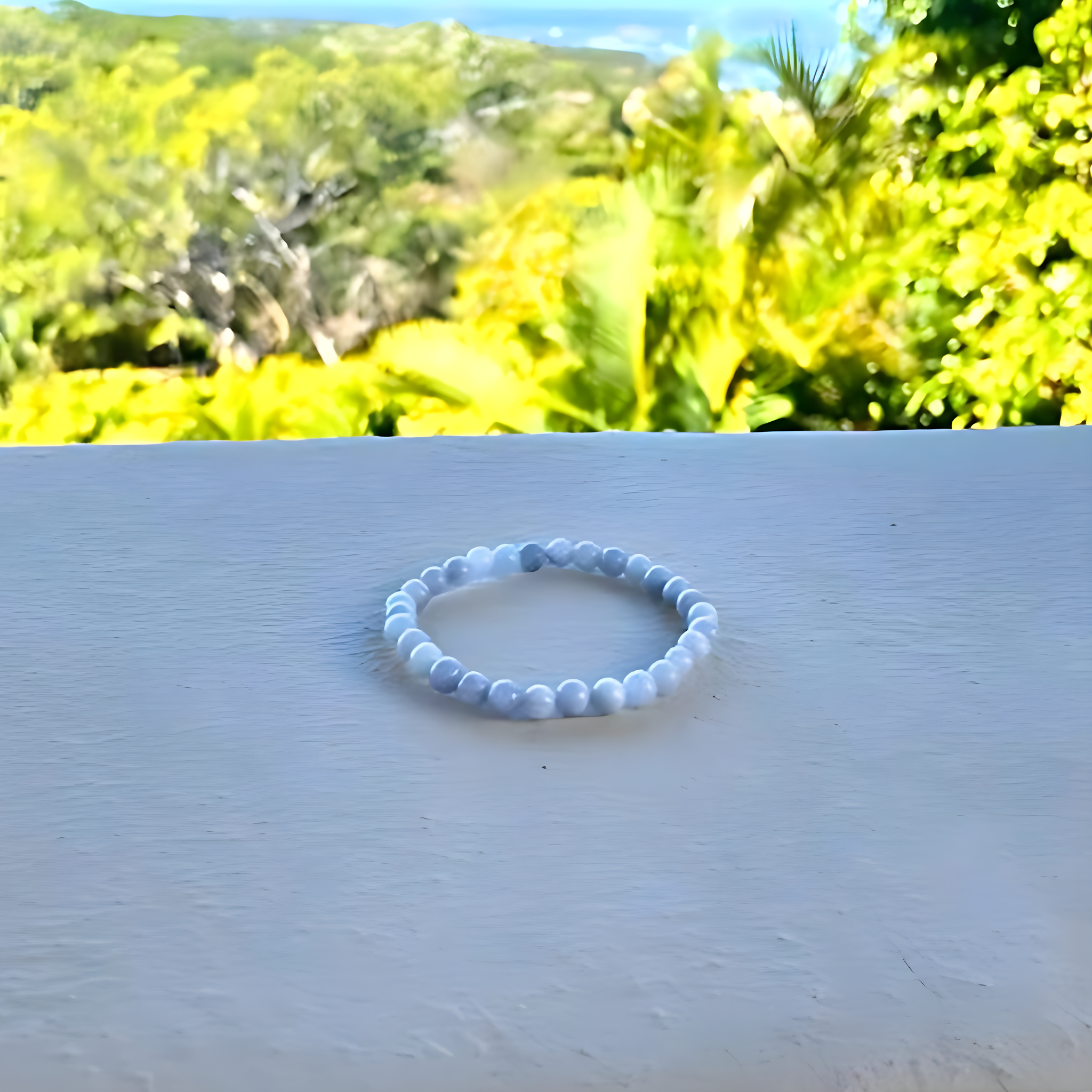 Blue beaded bracelet on a white surface with a blurred natural background