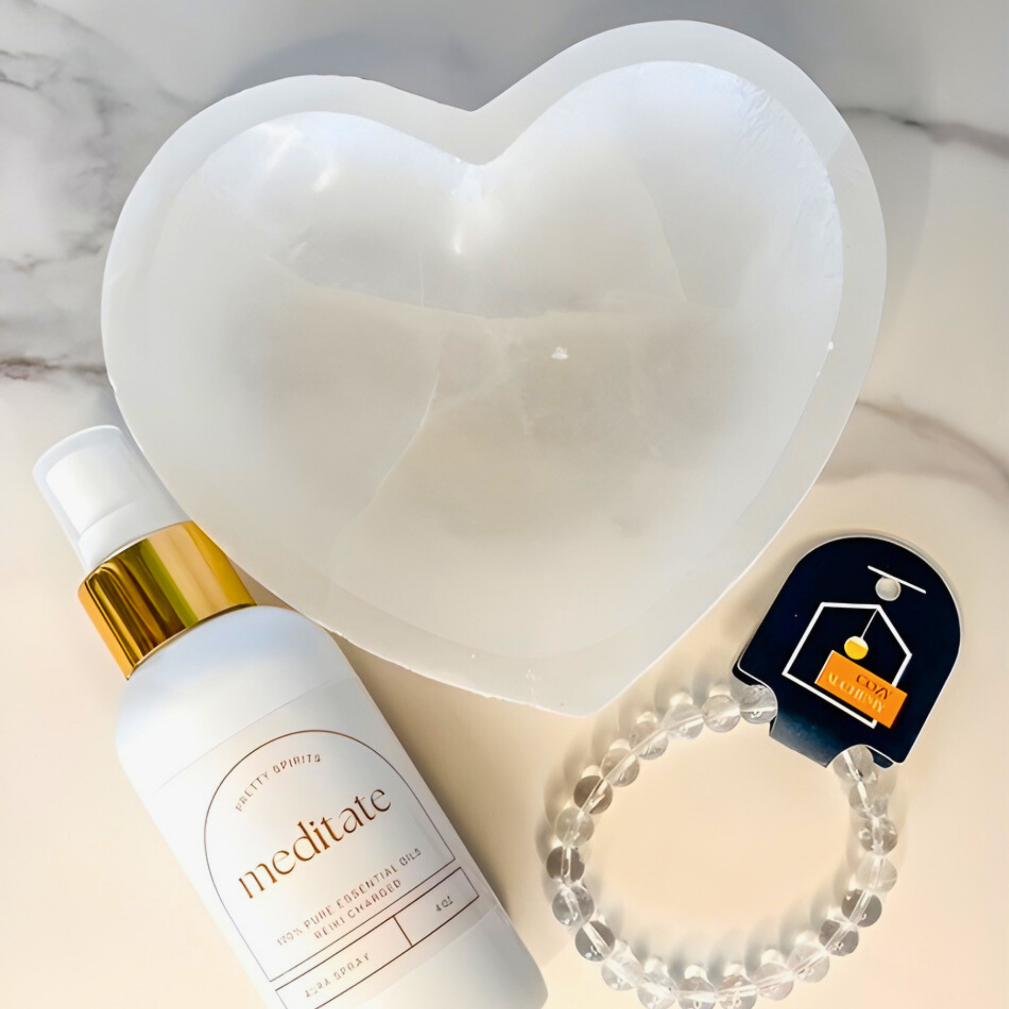 Heart-shaped dish with a bottle labeled 'meditate', bracelet, and small card on a marble surface.