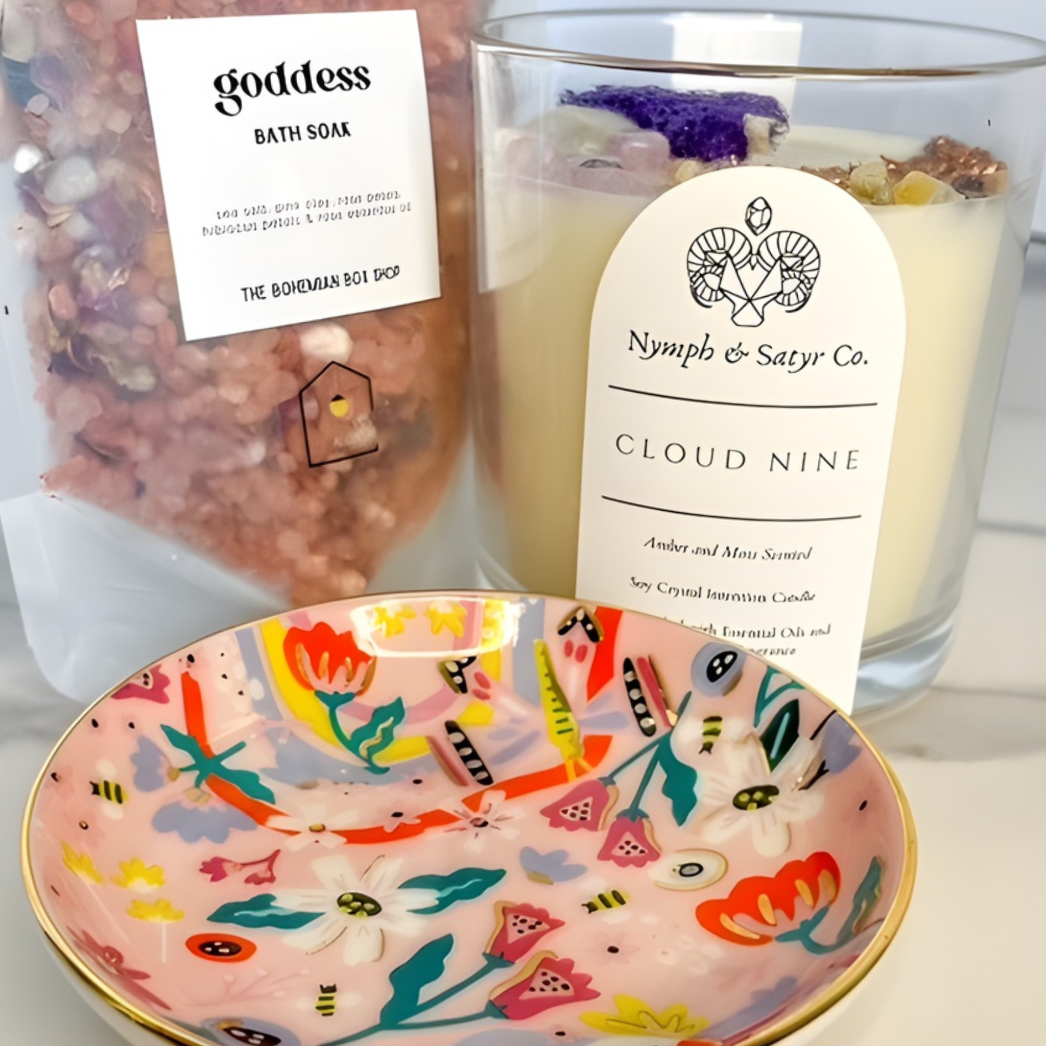 Candle labeled 'Cloud Nine' from Nymph & Satyr Co., bath soak, and decorative bowl on a white surface.