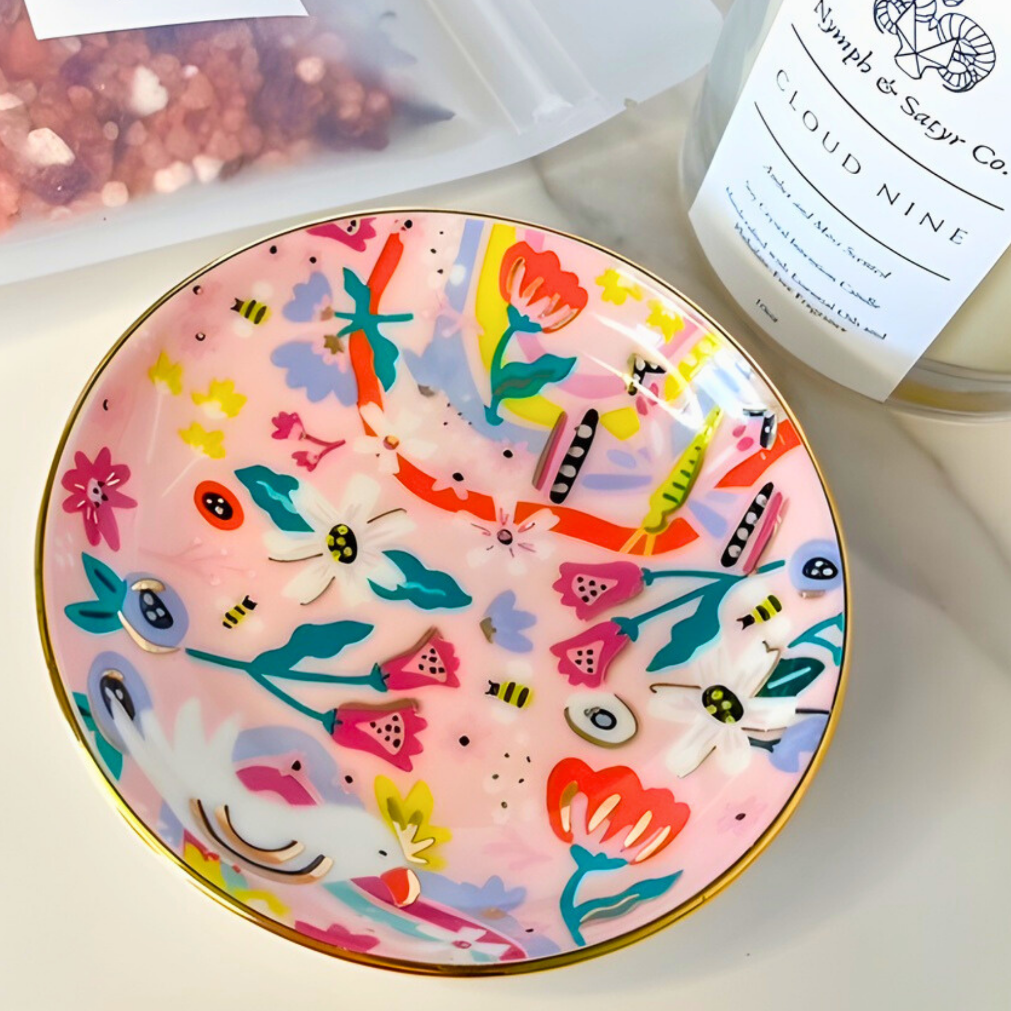 Decorative plate with colorful floral design on a white surface next to a candle labeled 'Cloud Nine'.