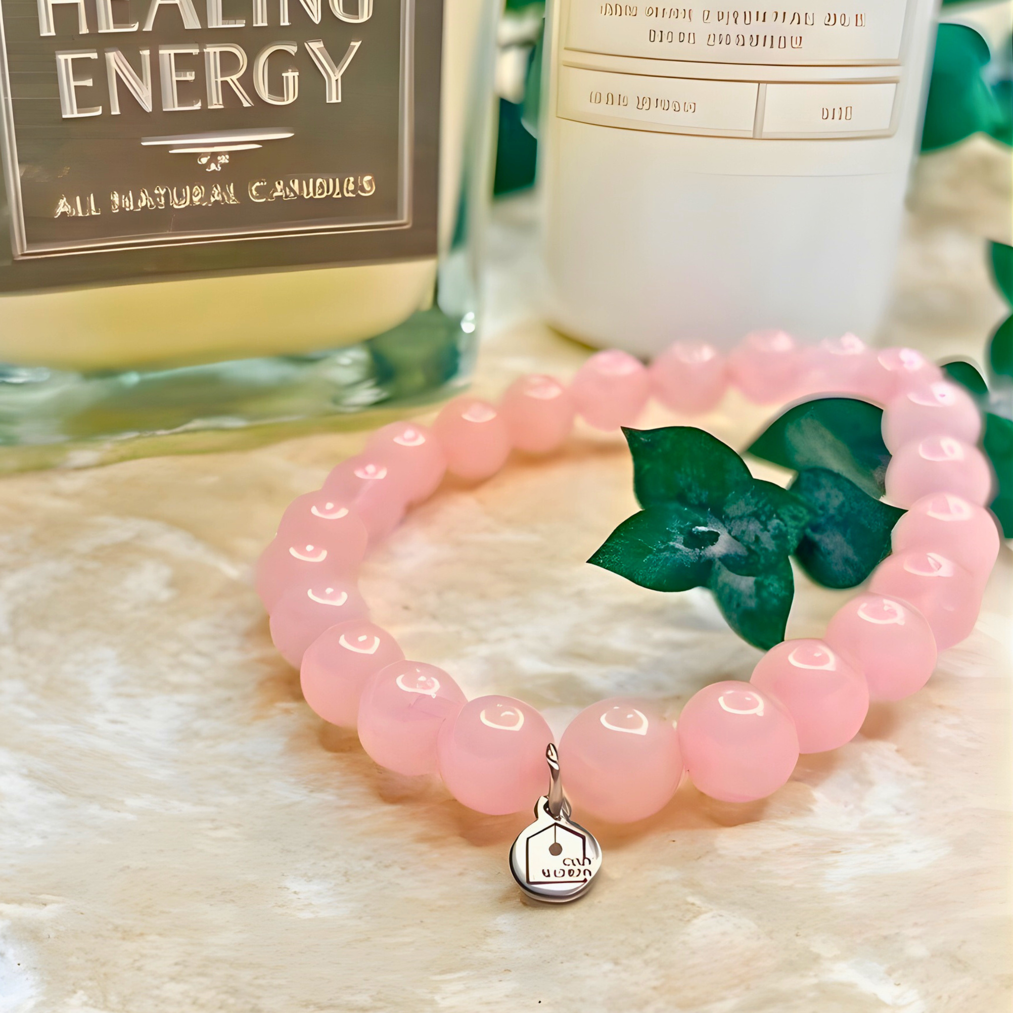 Pink beaded bracelet with a silver charm on a textured surface with a bottle in the background.