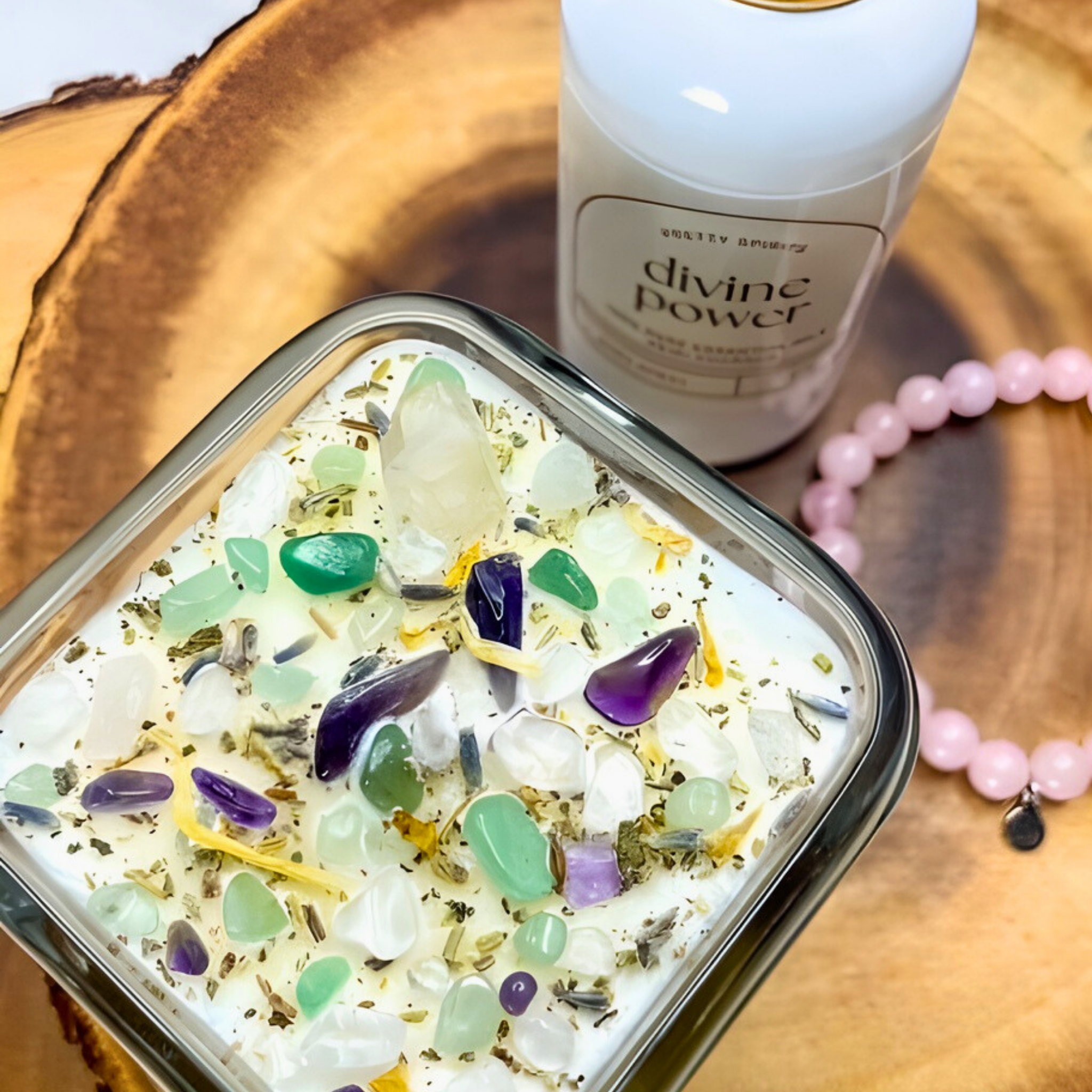 Candle with embedded stones on a wooden surface next to a bottle labeled 'divine power'.