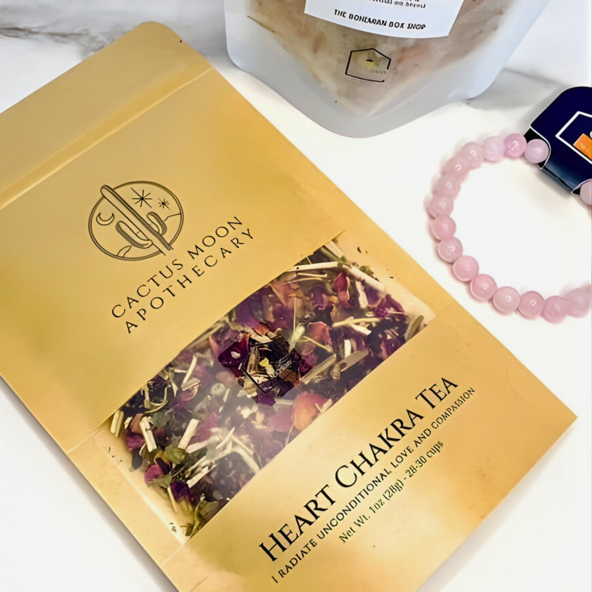Cactus Moon Apothecary Heart Chakra Tea package on a white surface with a bracelet and container.