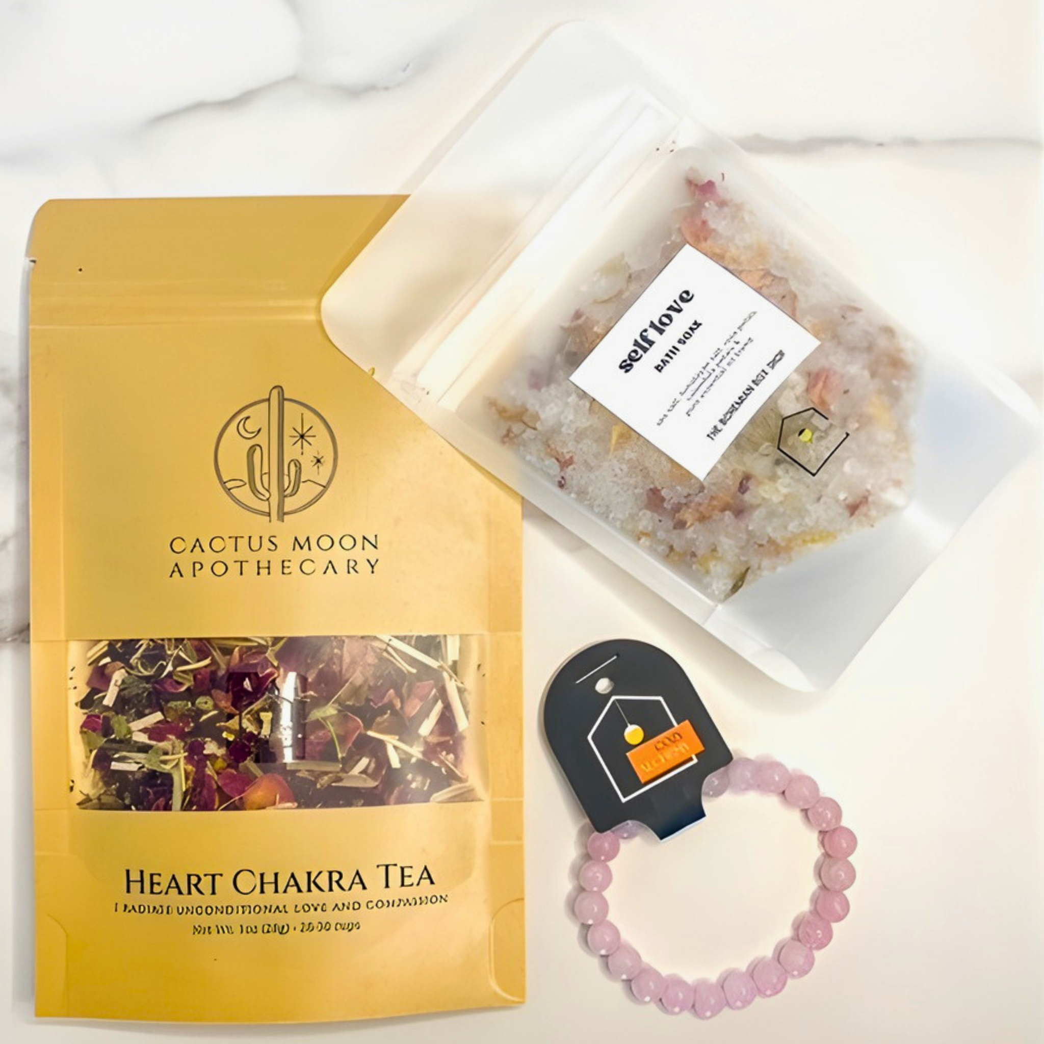 Cactus Moon Apothecary Heart Chakra Tea package, bath salts, and bracelet on a white marble surface