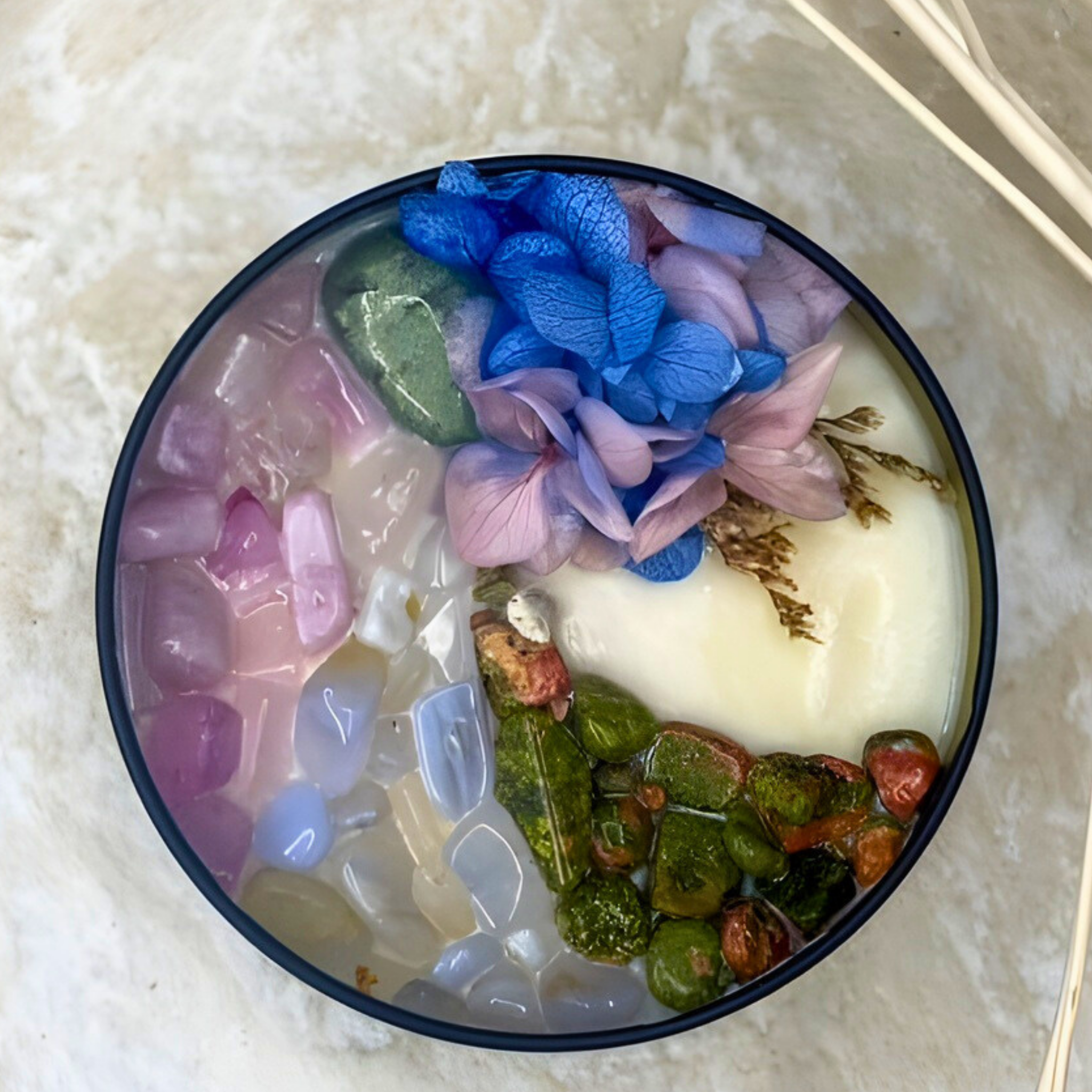 Decorative bowl with colorful stones and flowers on a textured surface