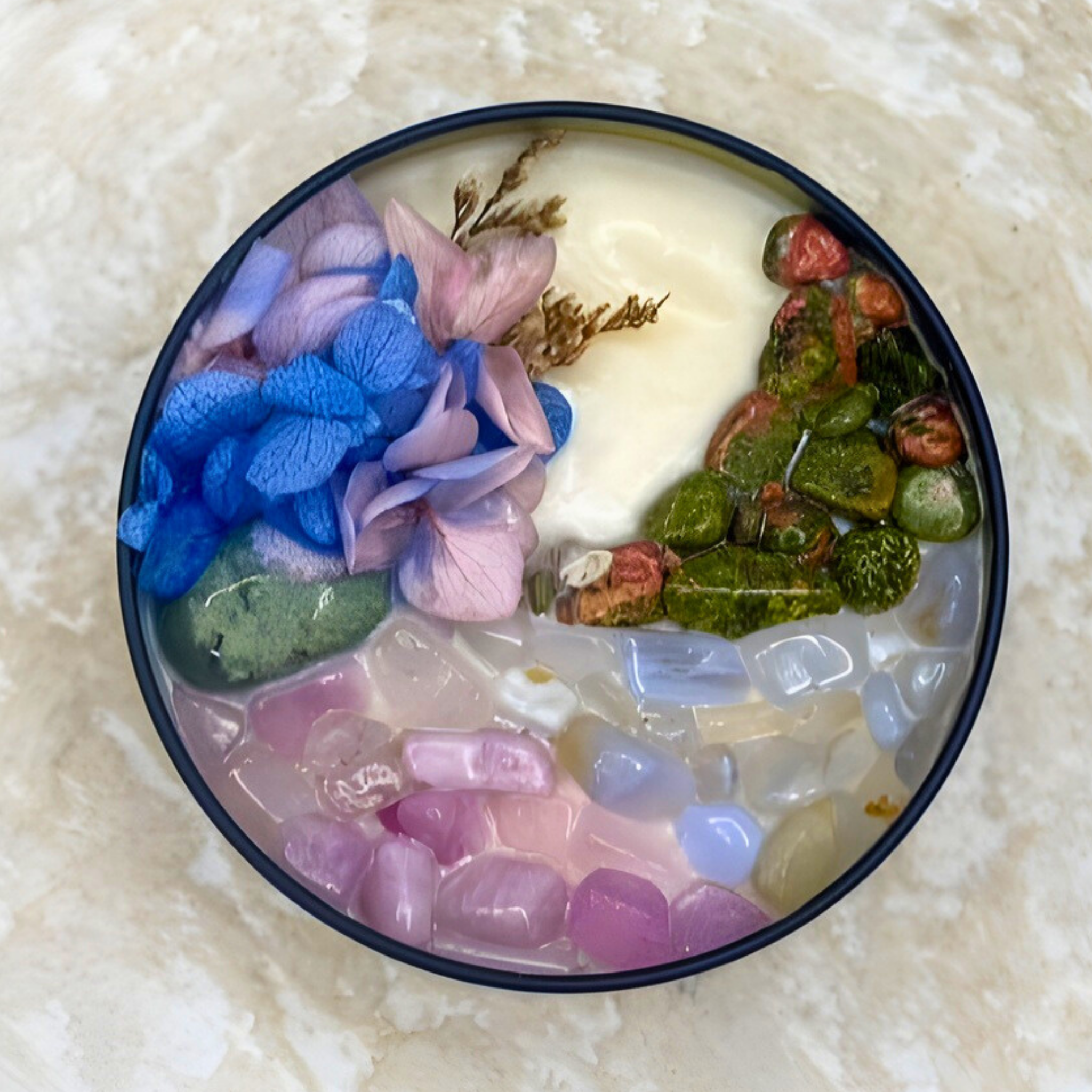 Decorative dish with colorful stones and flowers on a textured surface