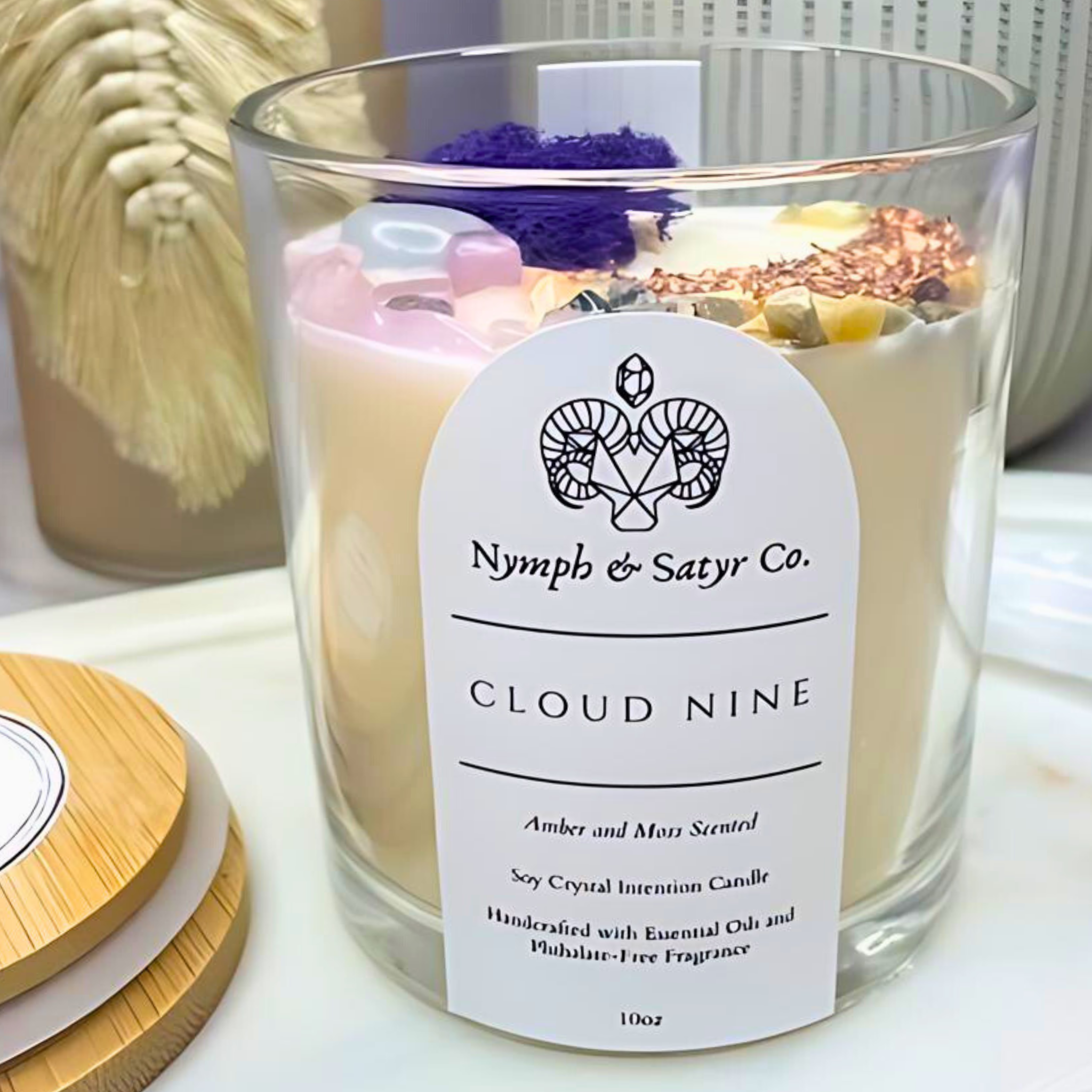 Candle labeled 'Nymph & Satyr Co. Cloud Nine' with decorative elements on a white surface.