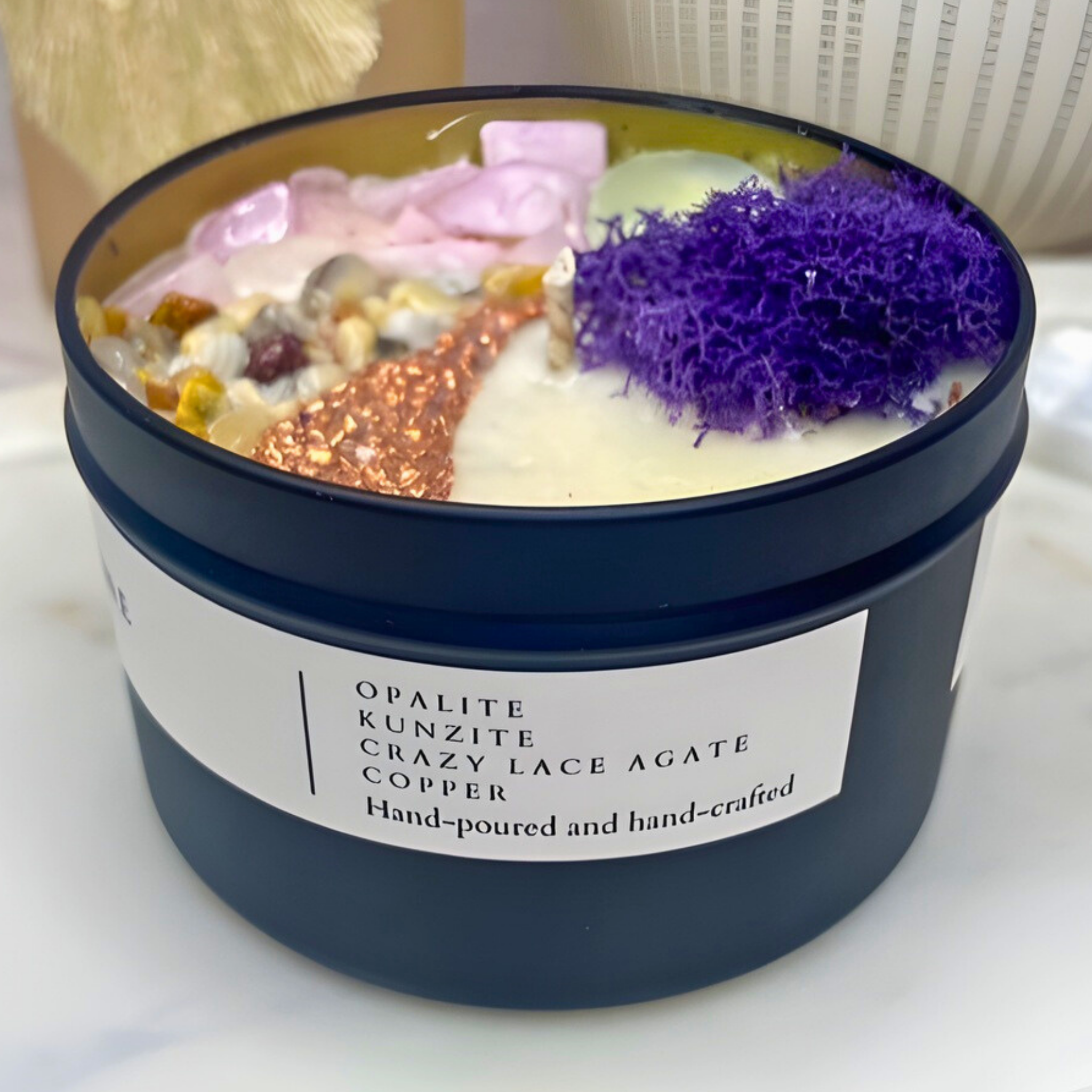 Candle in a navy container with decorative stones and a label on a white surface