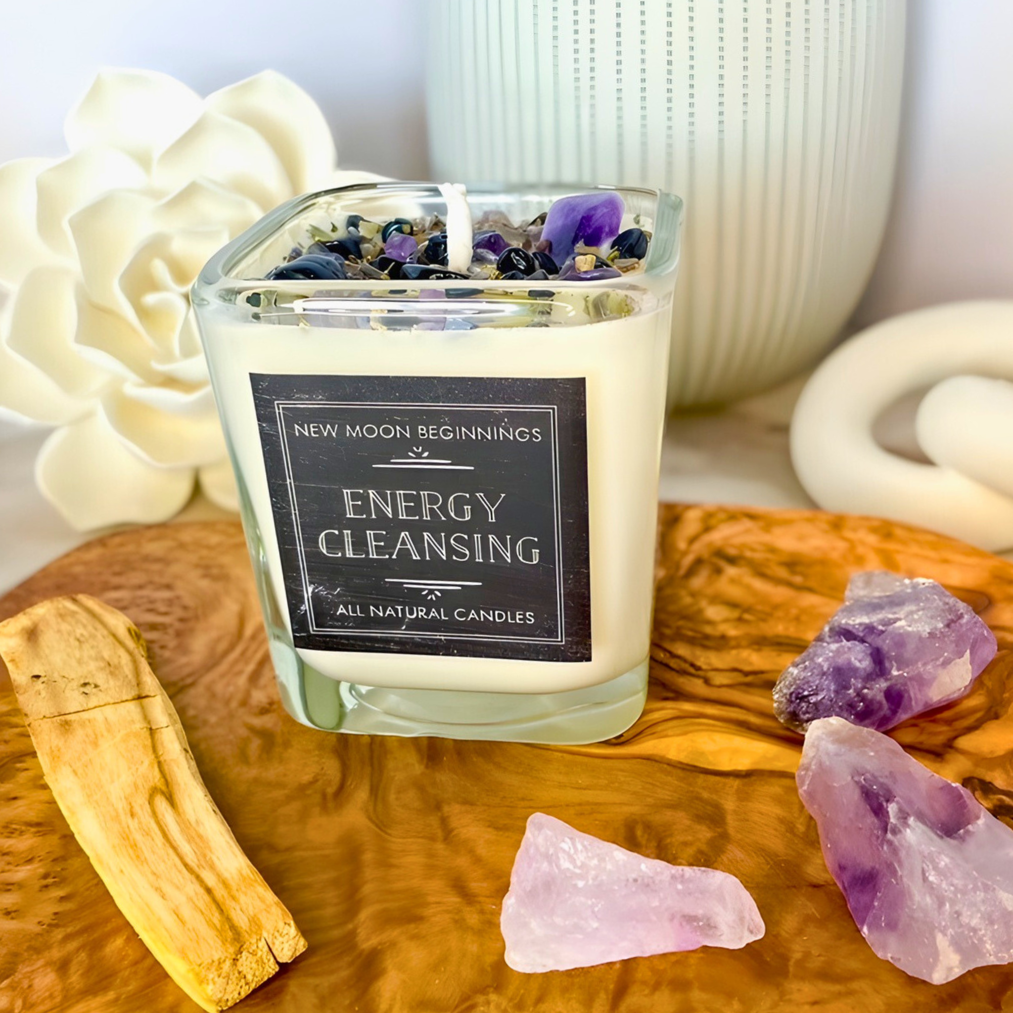 Candle labeled 'Energy Cleansing' with crystals and flowers on a wooden surface