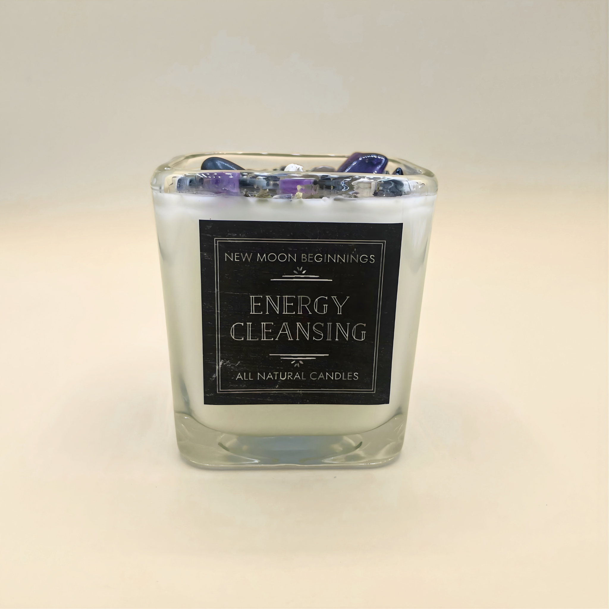 Candle labeled 'Energy Cleansing' by 'New Moon Beginnings' on a light background