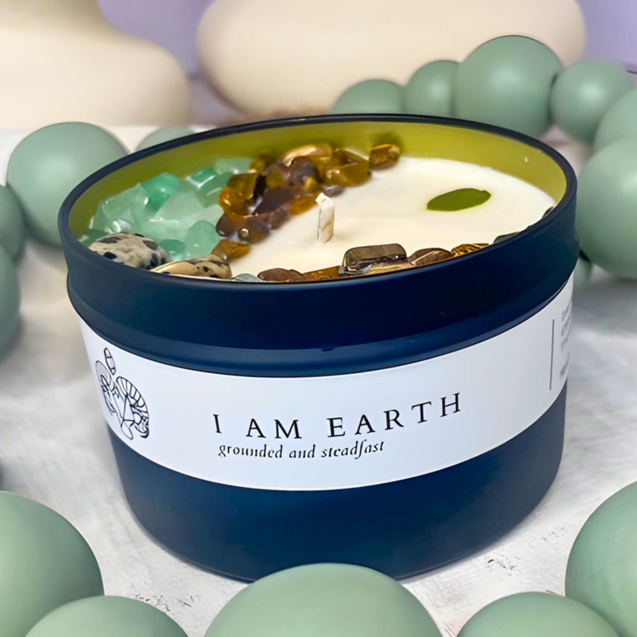 Candle jar labeled 'I AM EARTH' with decorative stones on a neutral background