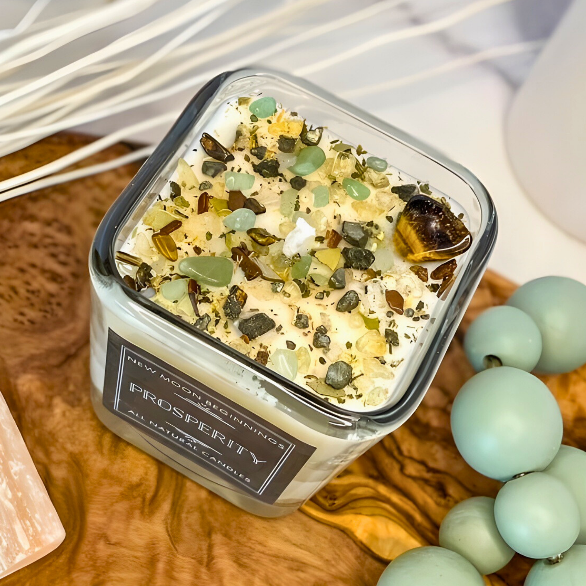 Candle jar labeled 'Prosperity' with decorative stones on a wooden surface.