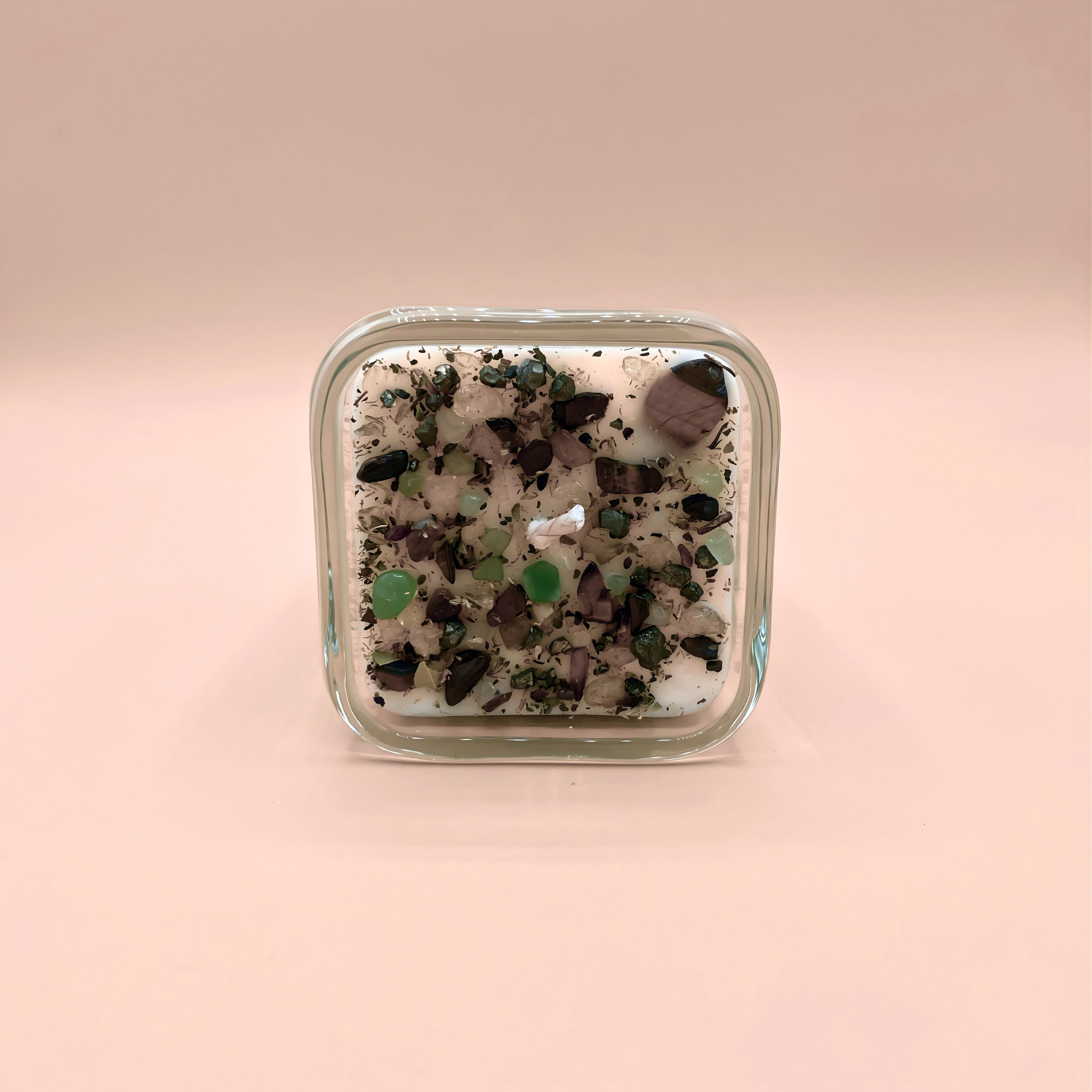 Square glass container with decorative stones on a pink background