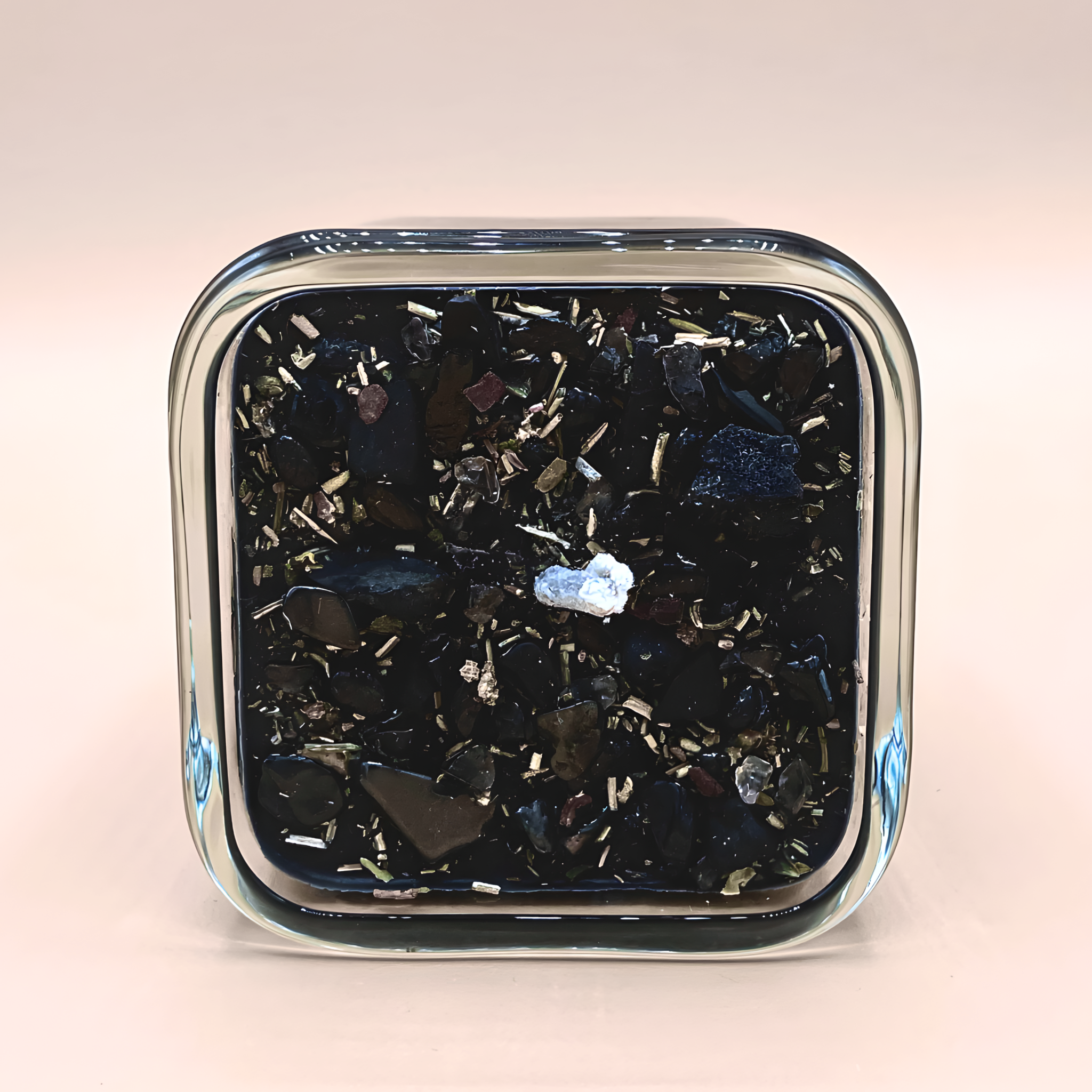 Square glass container with black and silver decorative stones on a light pink background