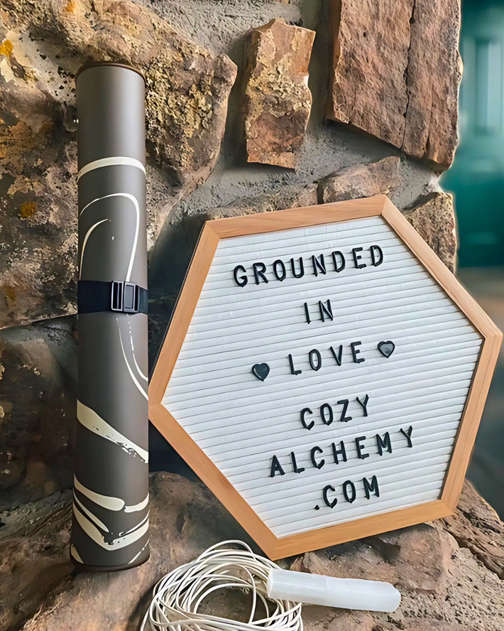 Hexagonal letter board with text 'Grounded in Love Cozy Alchemy.com' next to a cylindrical product on a stone surface.