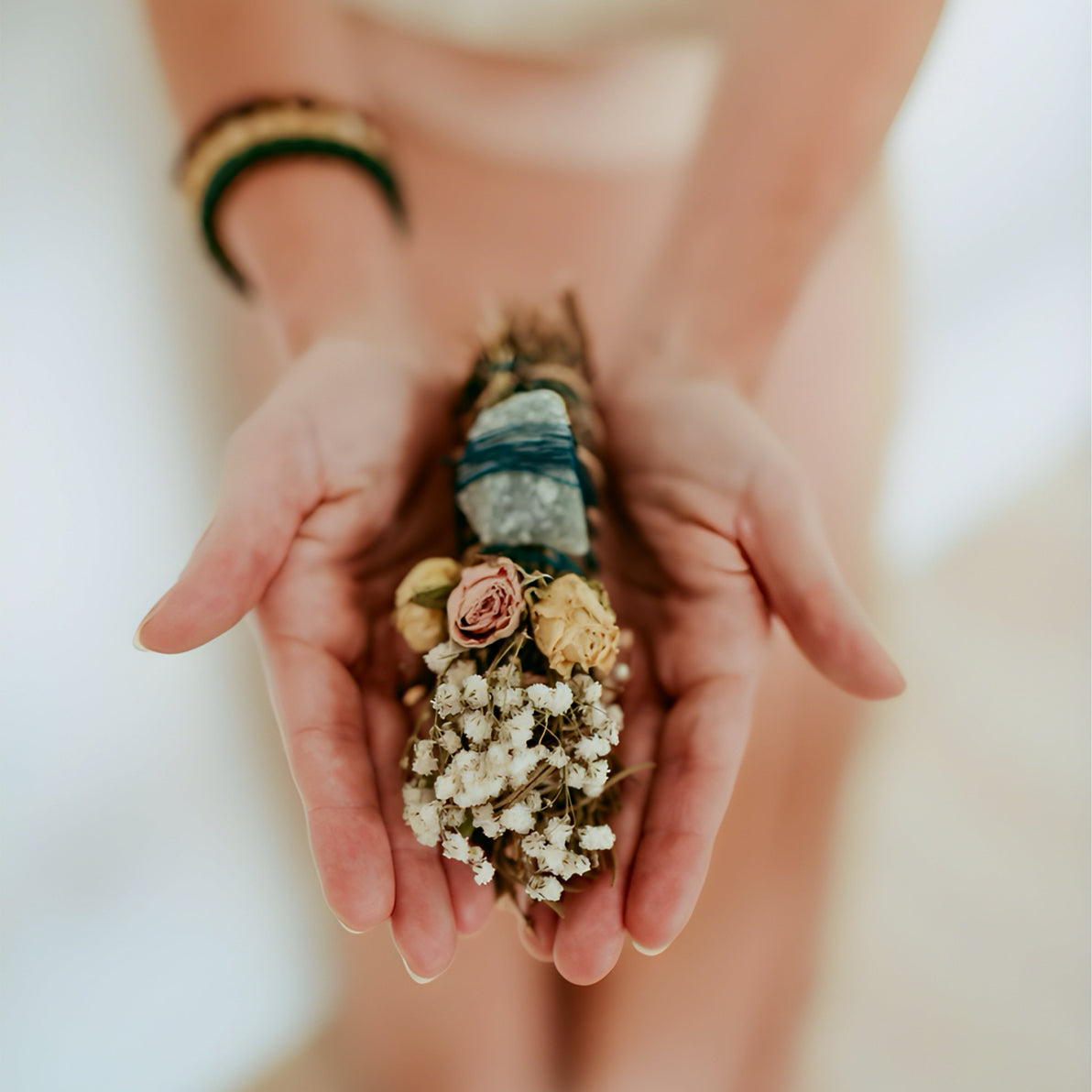 Hands holding small flowers and stones against a blurred background