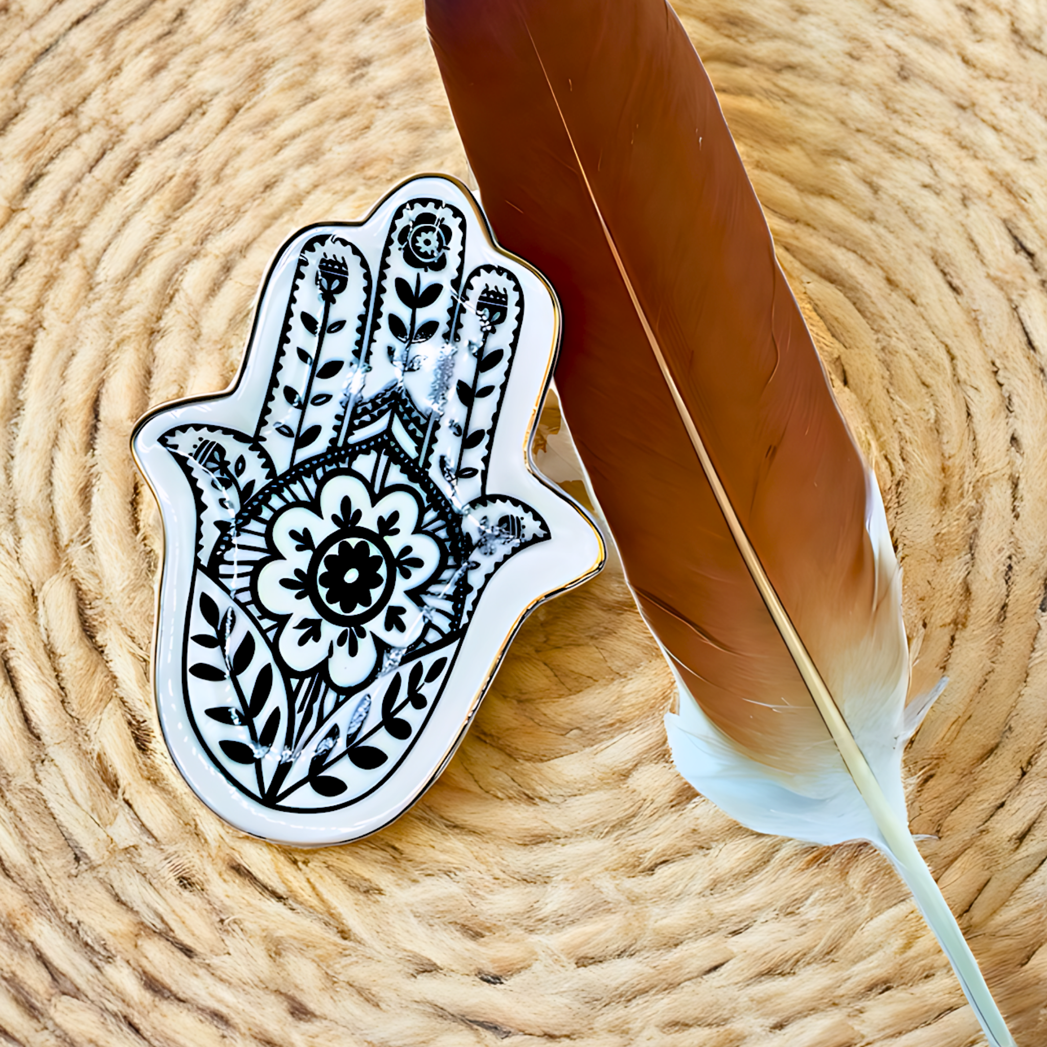 Decorative Hamsa hand with intricate patterns on a woven surface with a feather.