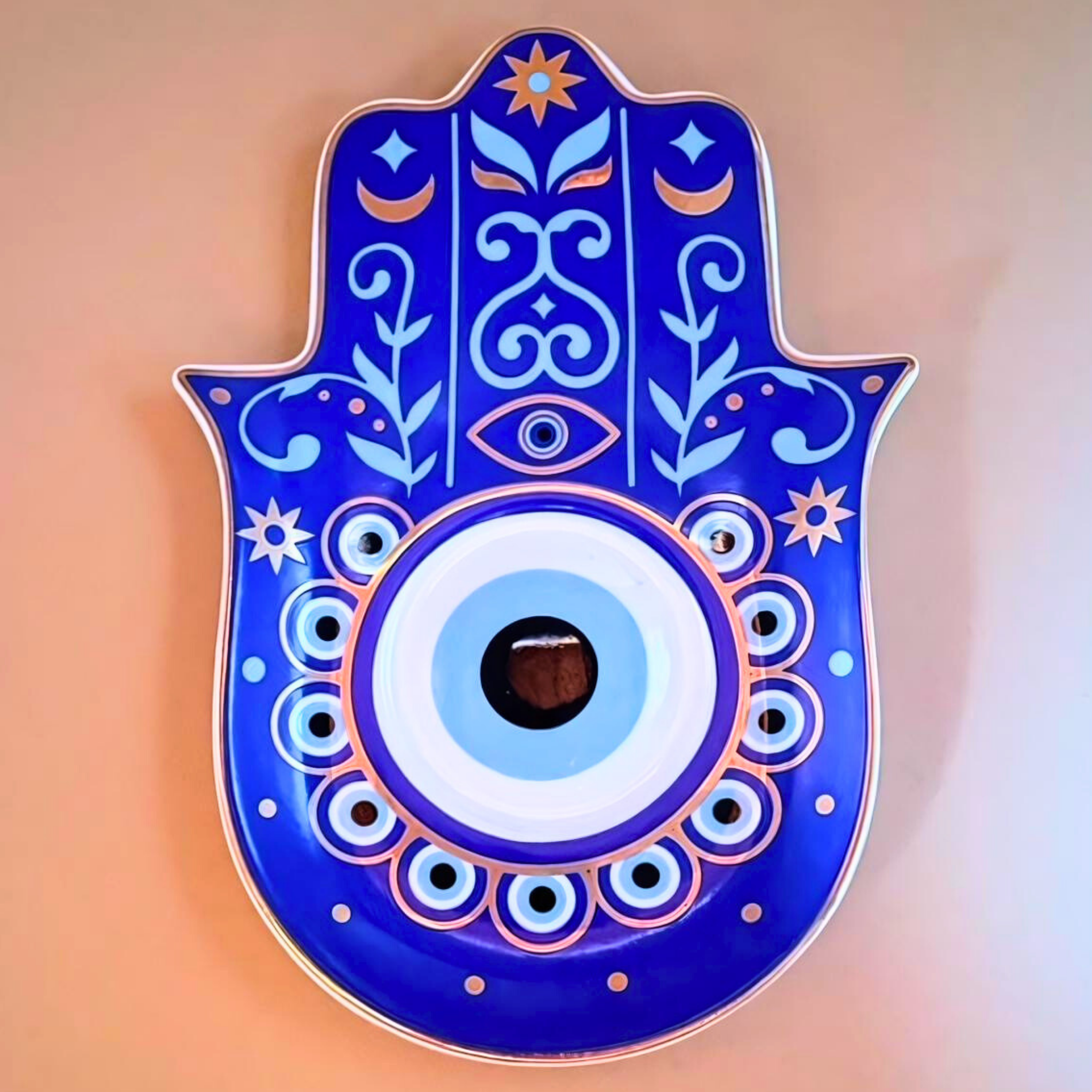 Decorative Hamsa hand with blue and white patterns on a peach background