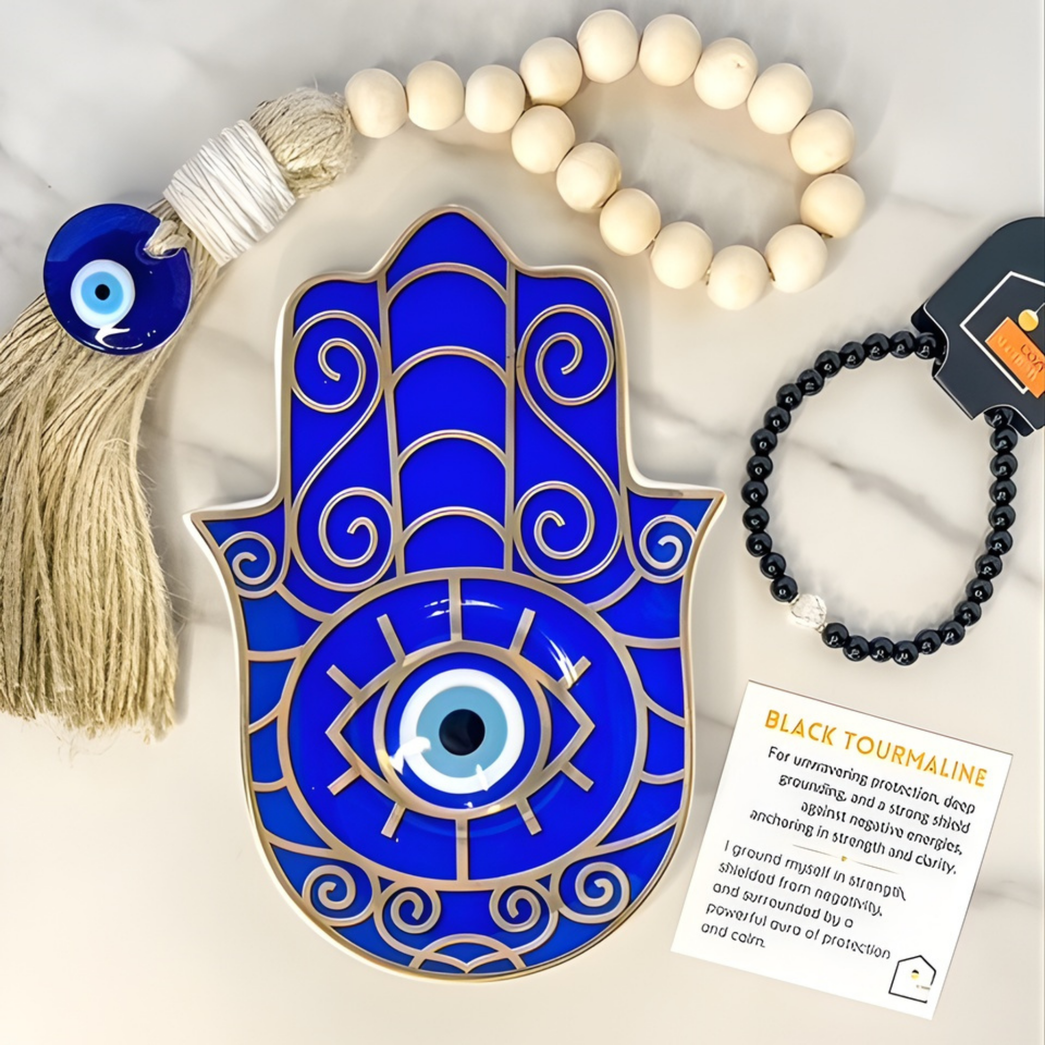 Blue Hamsa hand with evil eye, tassel, beads, and black tourmaline bracelet on a light background