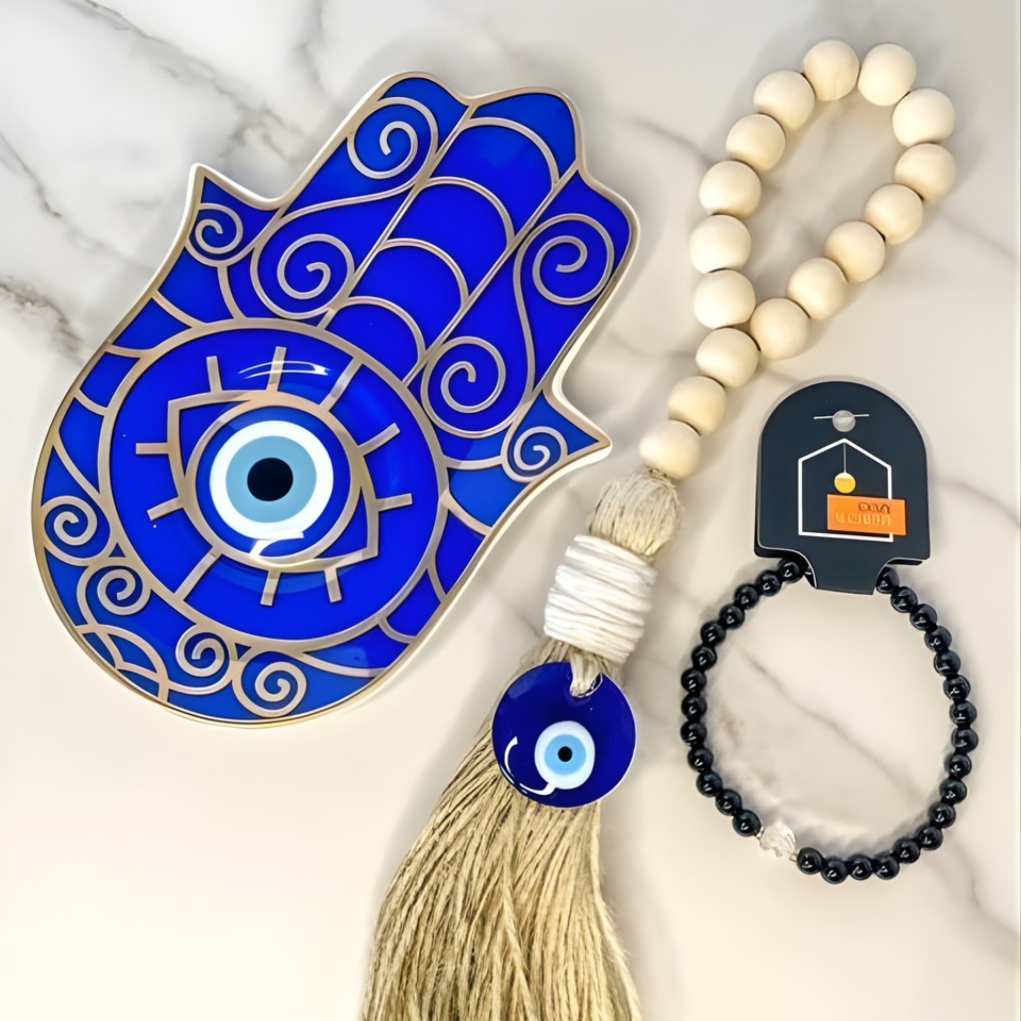Blue Hamsa hand with tassel, white beaded necklace, and black beaded bracelet on a marble surface.