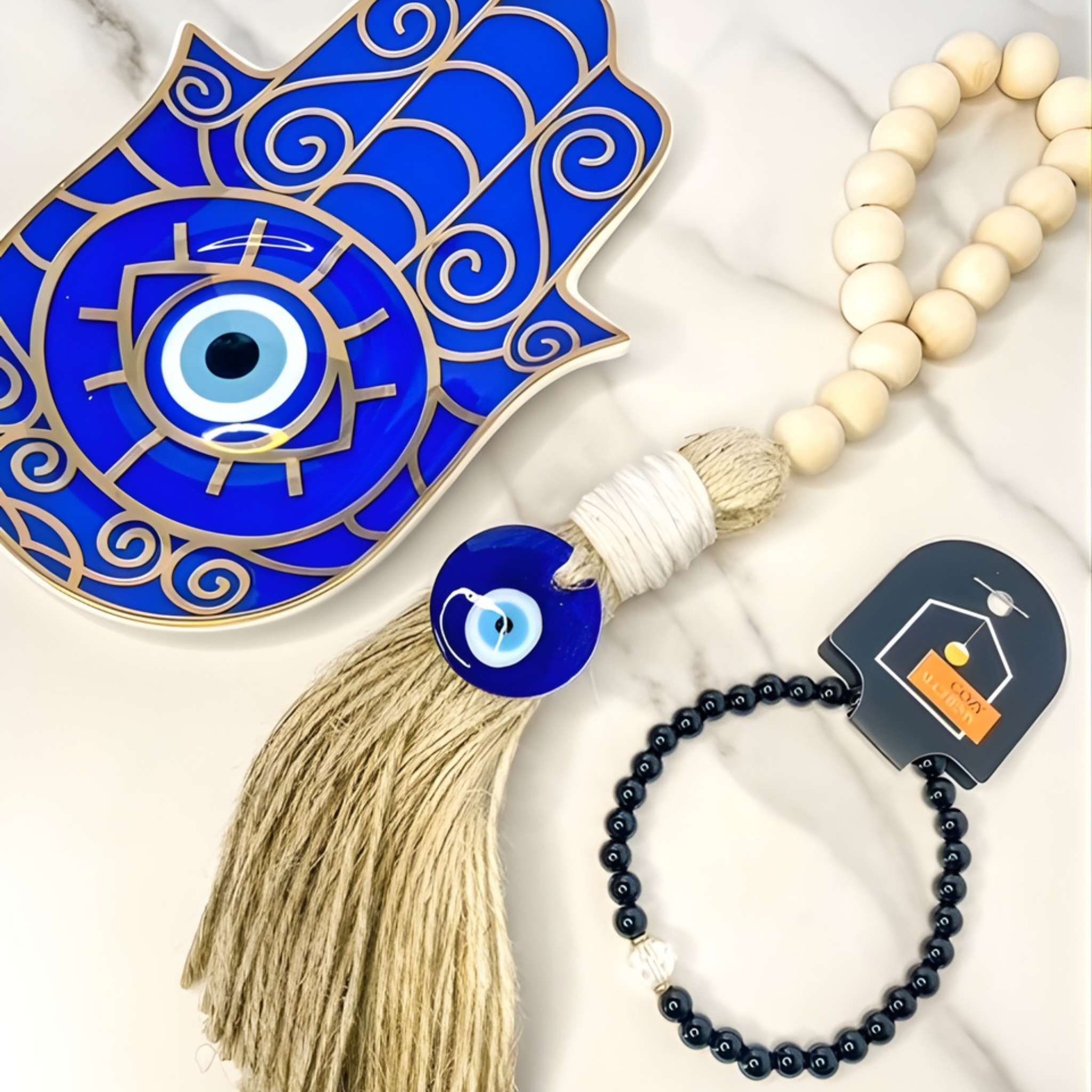 Blue evil eye tassel with a white beaded bracelet and black beaded bracelet on a light background