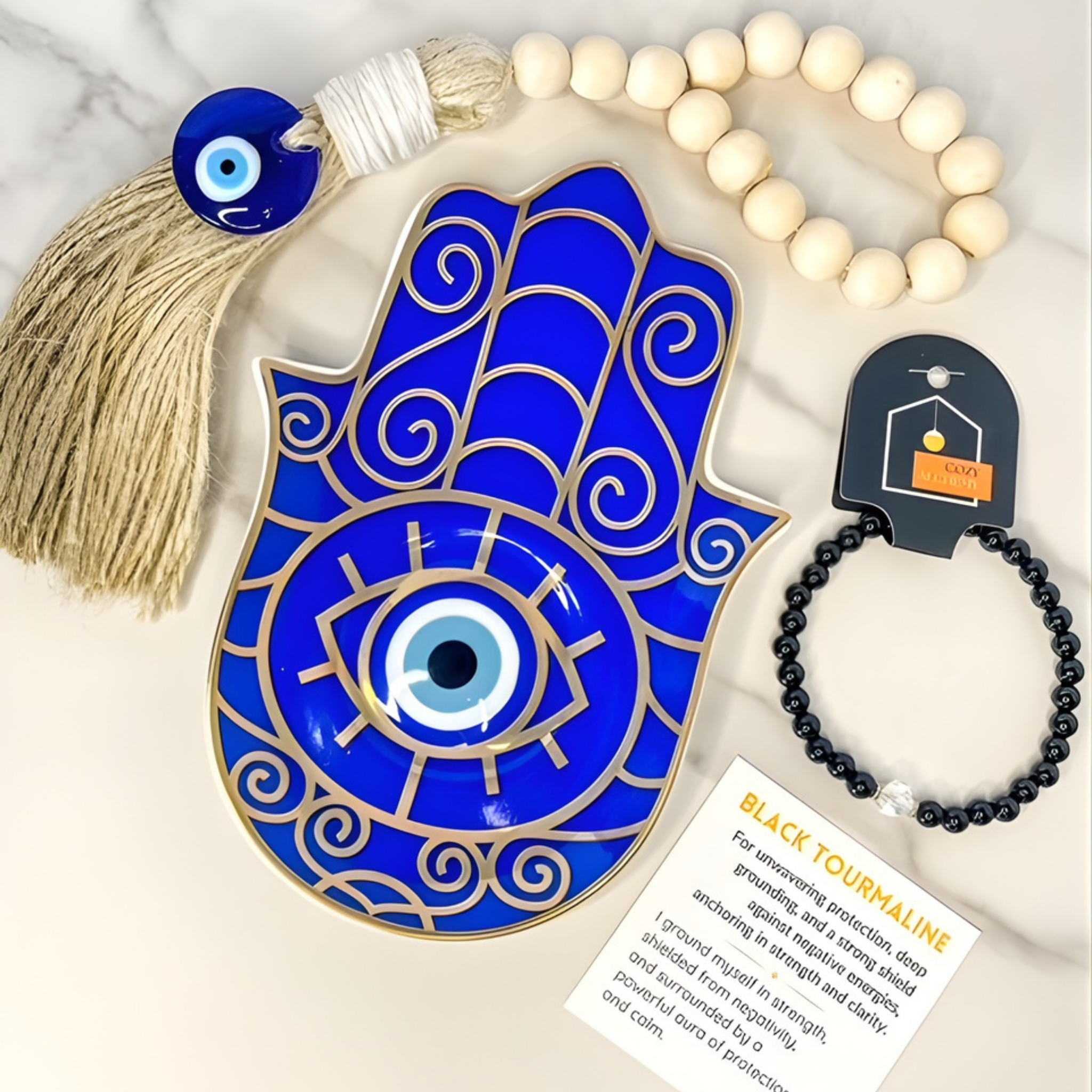 Blue Hamsa hand with tassel, black tourmaline bracelet, and card on a light background