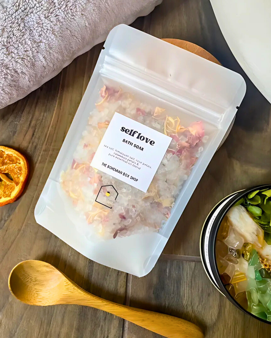 Packaged bath soap with 'self love' label on a wooden surface with a spoon and dried orange.