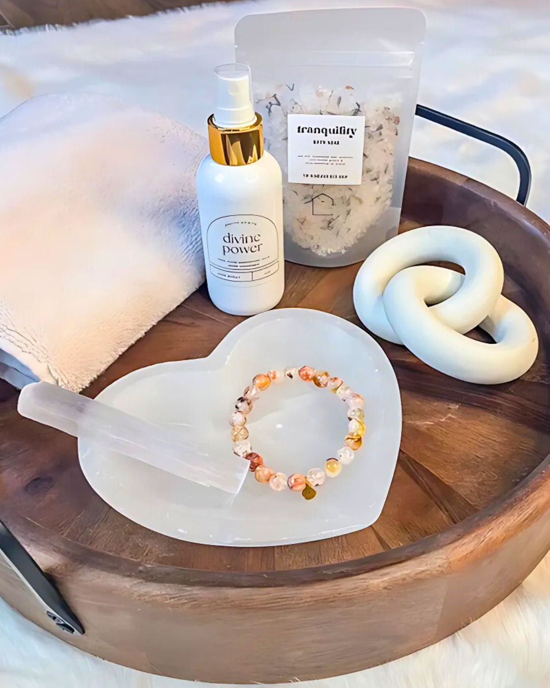 Tranquility product, bottle labeled 'divine power', bracelet on a white dish, towel, and wooden tray.