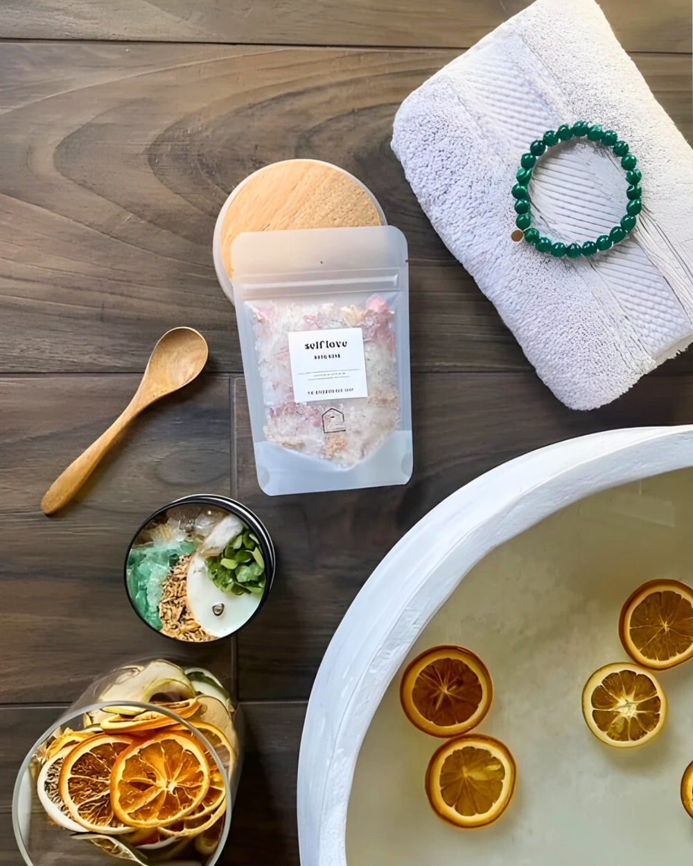Bath setup with bath salts, oranges, towel, and spoon on a wooden surface