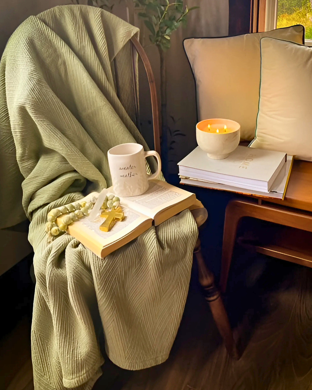 Cozy indoor setting with a green blanket, mug, book, and small bowl on a chair.