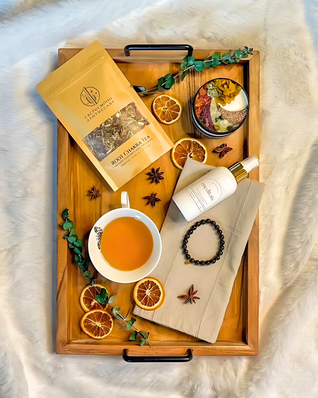 Wooden tray with tea, oranges, and wellness items on a soft surface